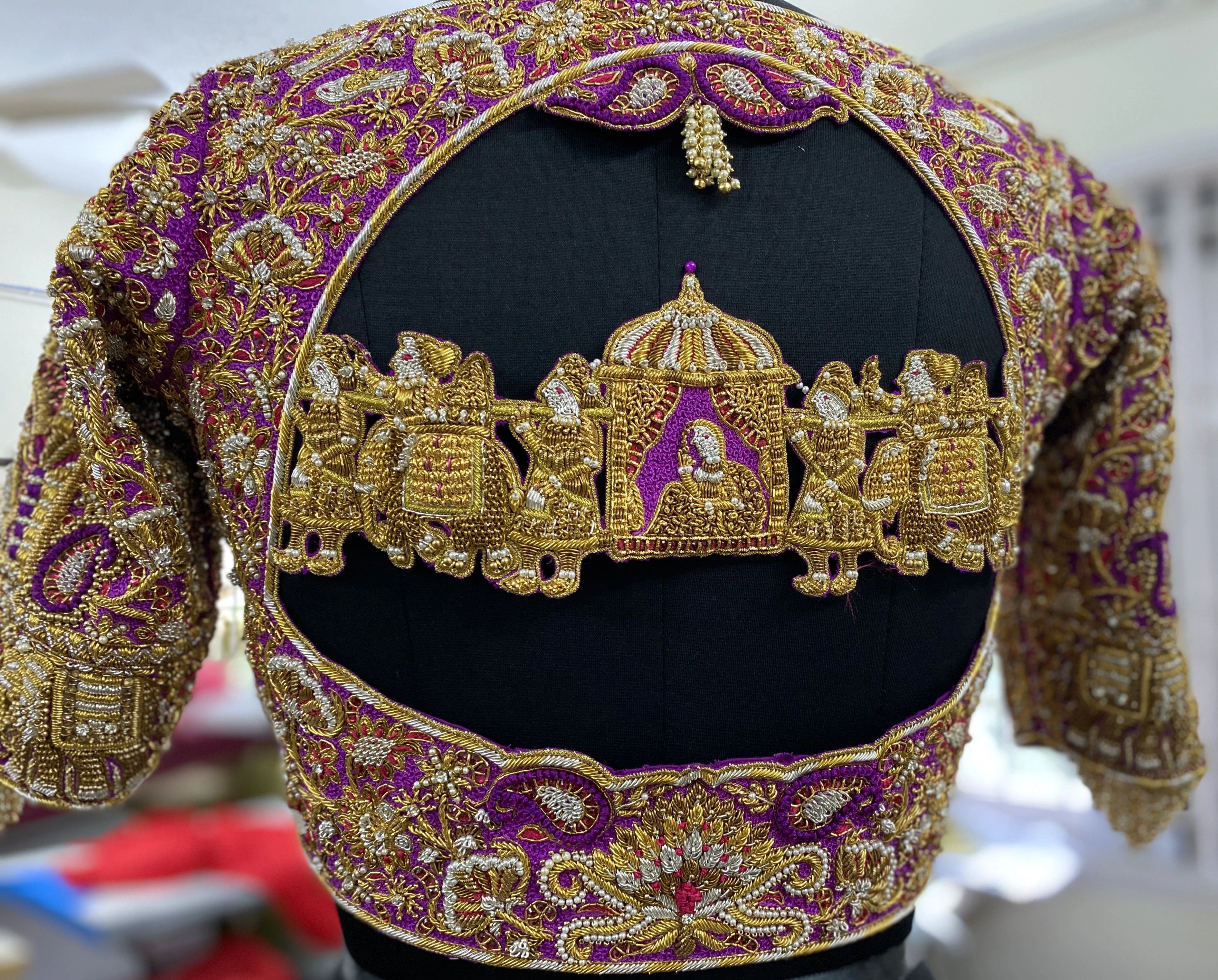 A handcrafted palanquin concept magenta pink silk blouse with zardozi, kemp stones, pearls and resham knot work and goddess pendants on each sleeve. Designed by Archana Karthick