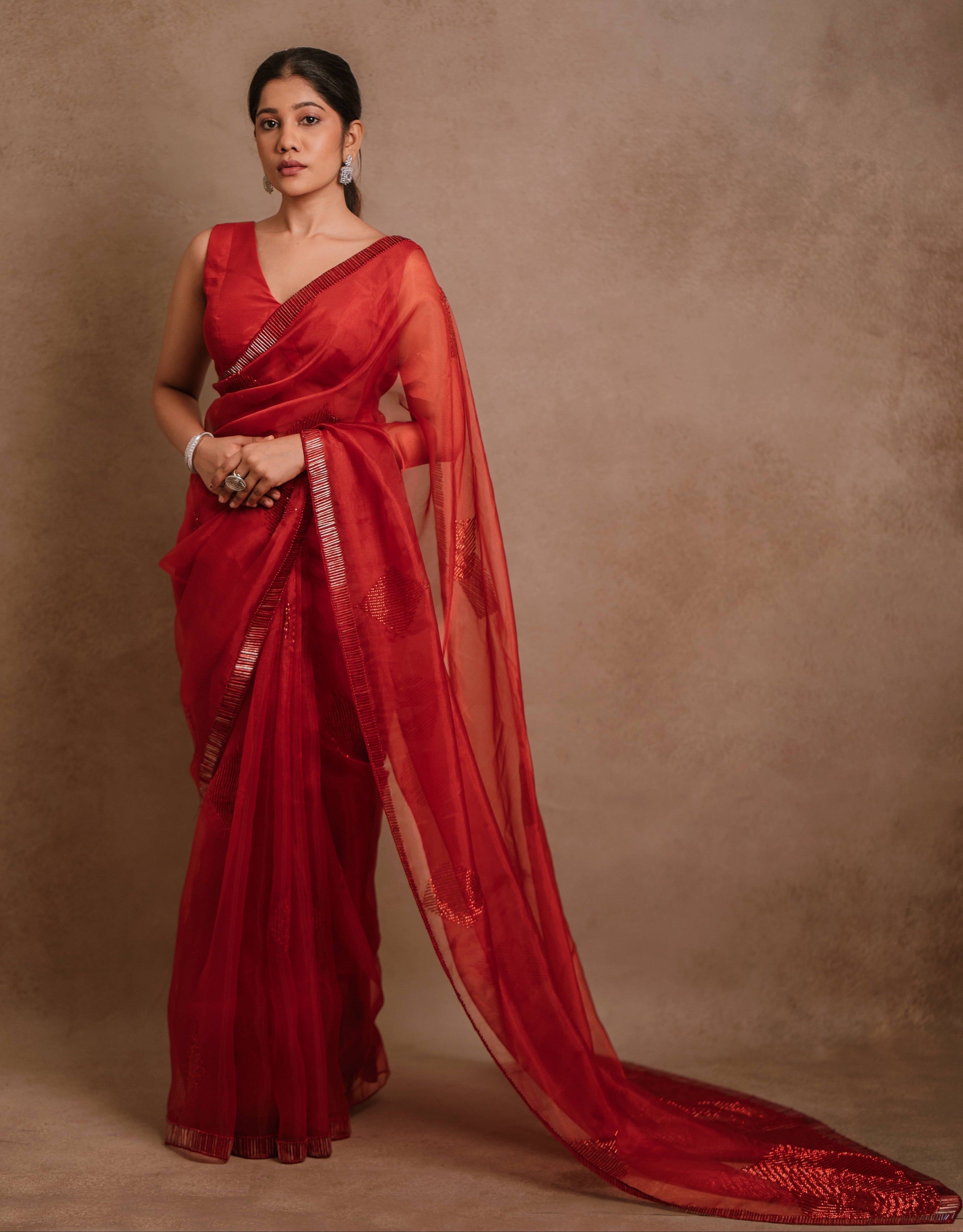 A red-orange organza saree intricately handcrafted with cutdana lines, designed by team Archana Karthick.