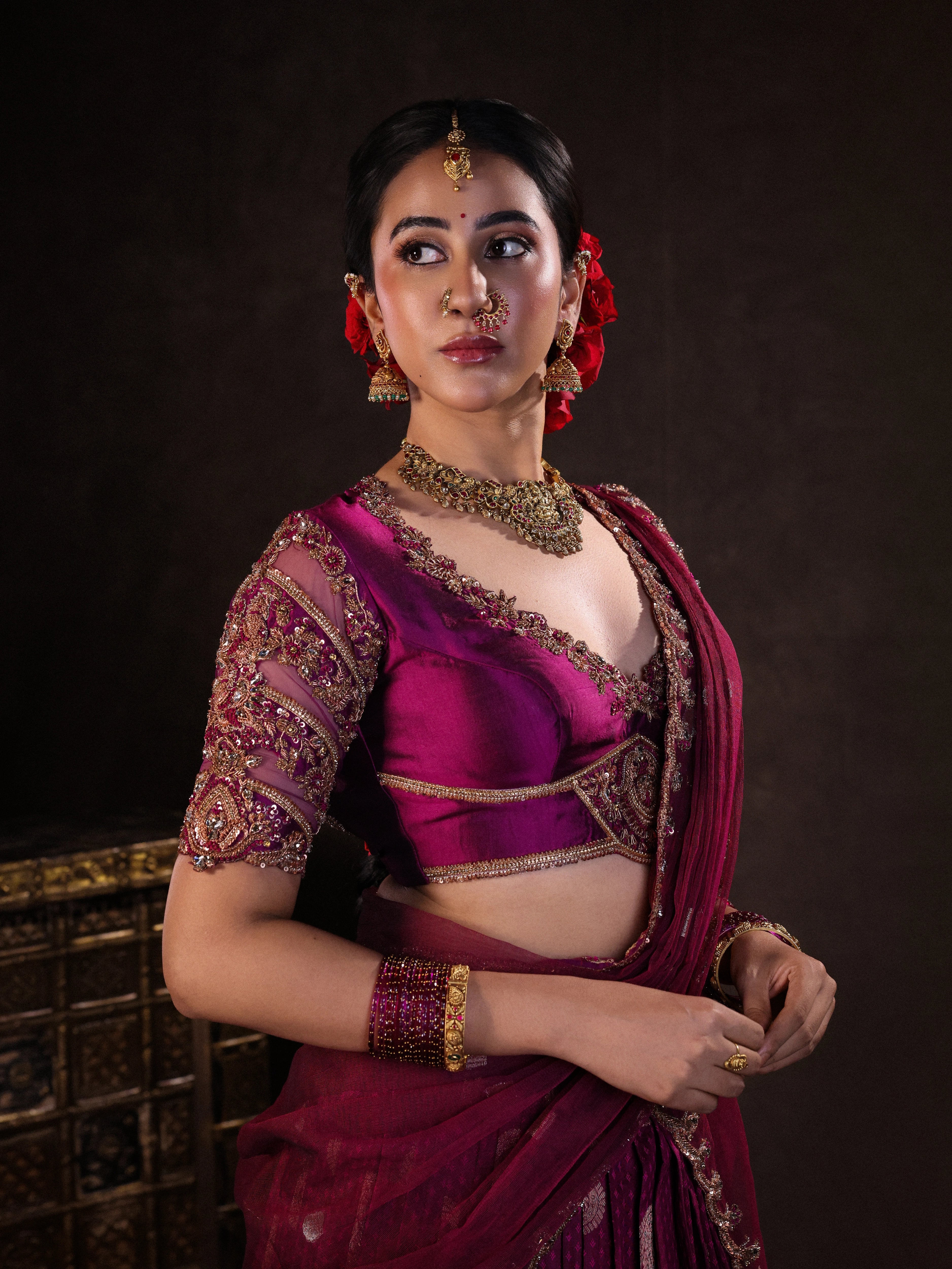 Actress Akshaya Hariharan posing during photoshoot in a dark magenta silk half saree set handcrafted with zardozi, resham, cutdana, sequins & rhinestones. Team Archana Karthick completed the style with dark magenta glass bangles, a ring, jhumkas, nose ring and a maang tikka.