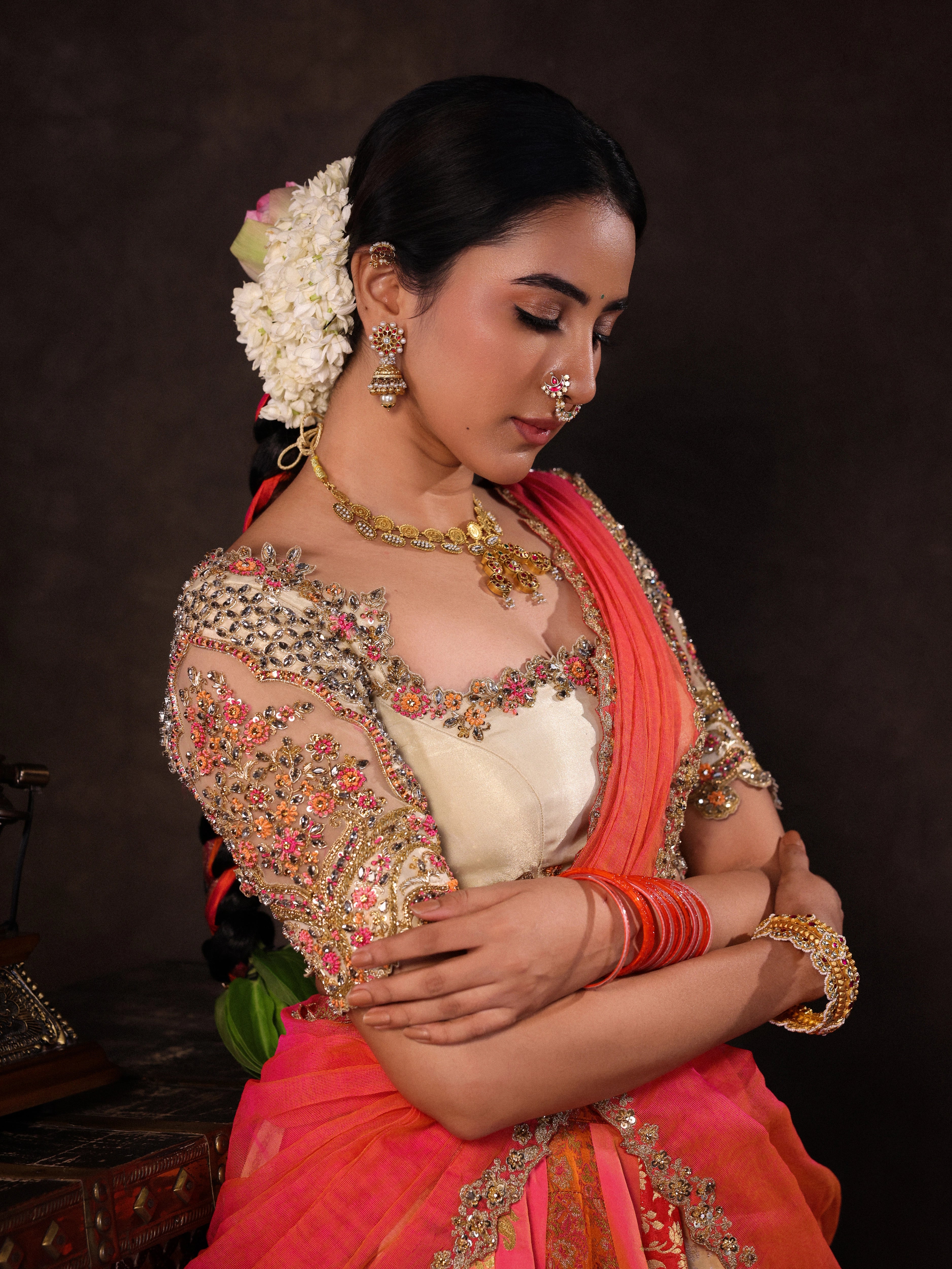 Actress Akshaya Hariharan posing for a closeup in an ivory & pink brocade half saree set with tulle sleeves & dupatta. Team Archana Karthick completed the style with purple glass bangles, a ring, jhumkas, nose ring and a maang tikka.
