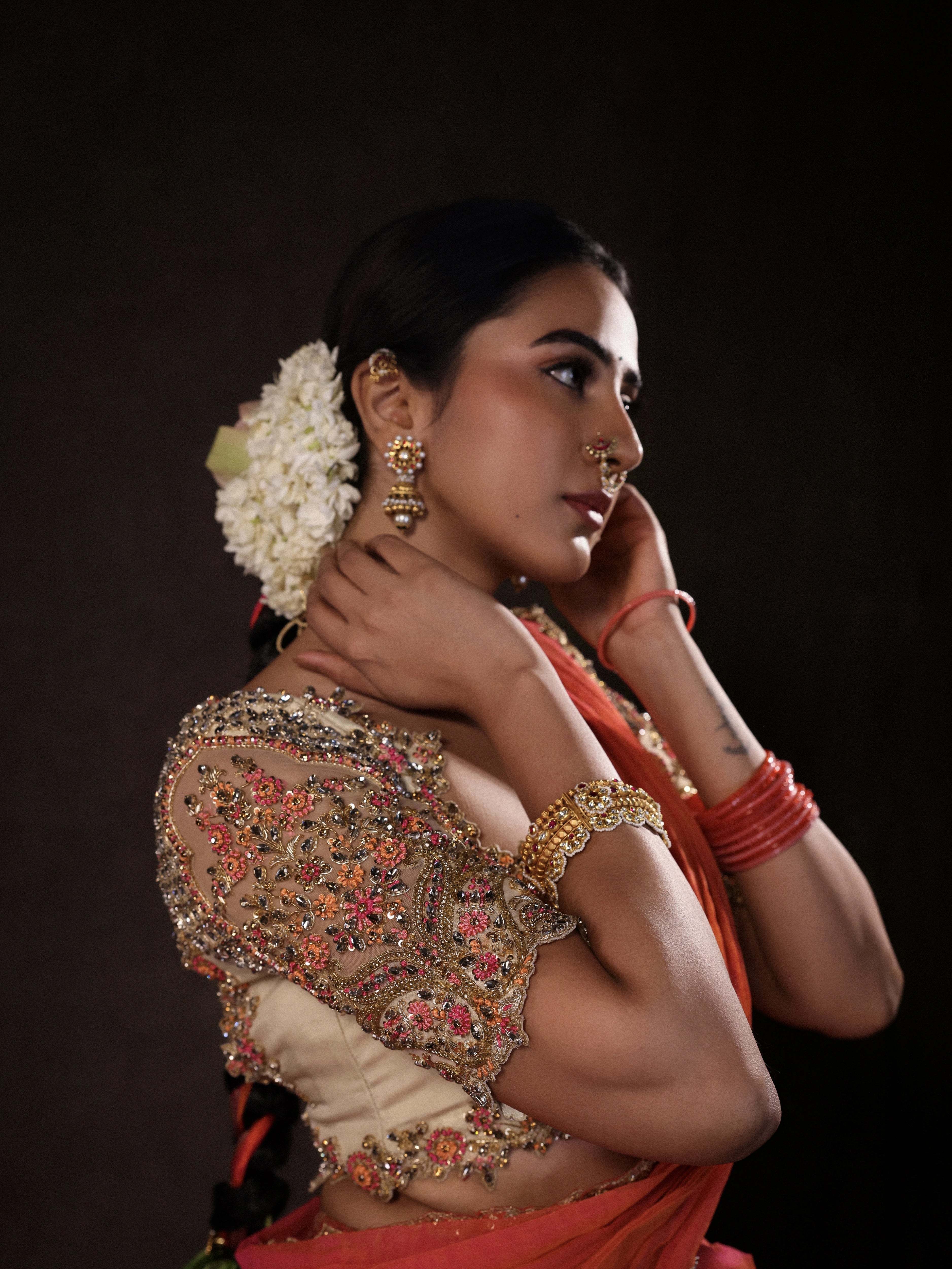 Actress Akshaya Hariharan posing for sleeve detailing in an ivory & pink brocade half saree set with tulle sleeves & dupatta. Team Archana Karthick completed the style with purple glass bangles, a ring, jhumkas, nose ring and a maang tikka.