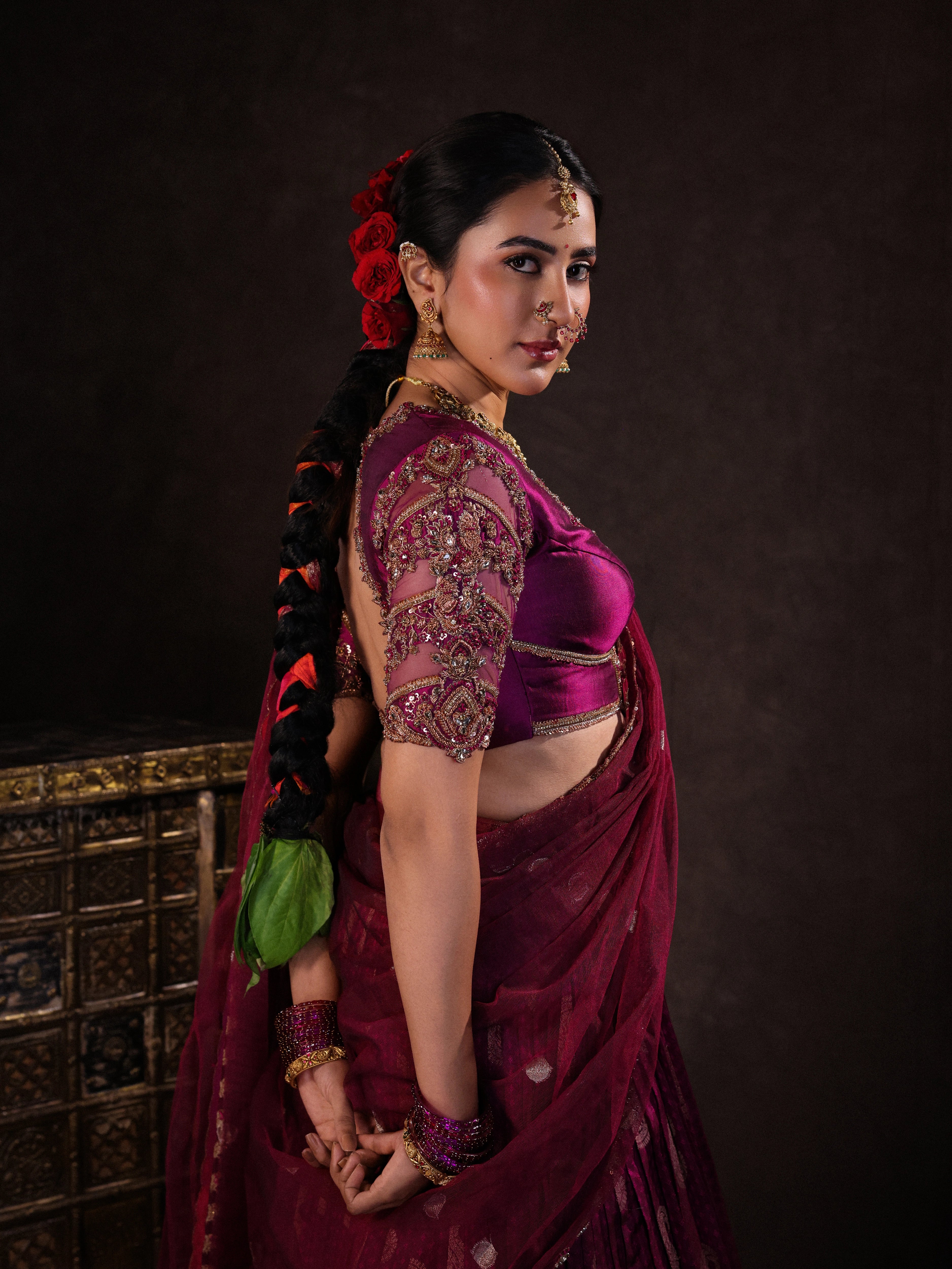 Actress Akshaya Hariharan smiling during photoshoot in a dark magenta silk half saree set handcrafted with zardozi, resham, cutdana, sequins & rhinestones. Team Archana Karthick completed the style with dark magenta glass bangles, a ring, jhumkas, nose ring and a maang tikka.
