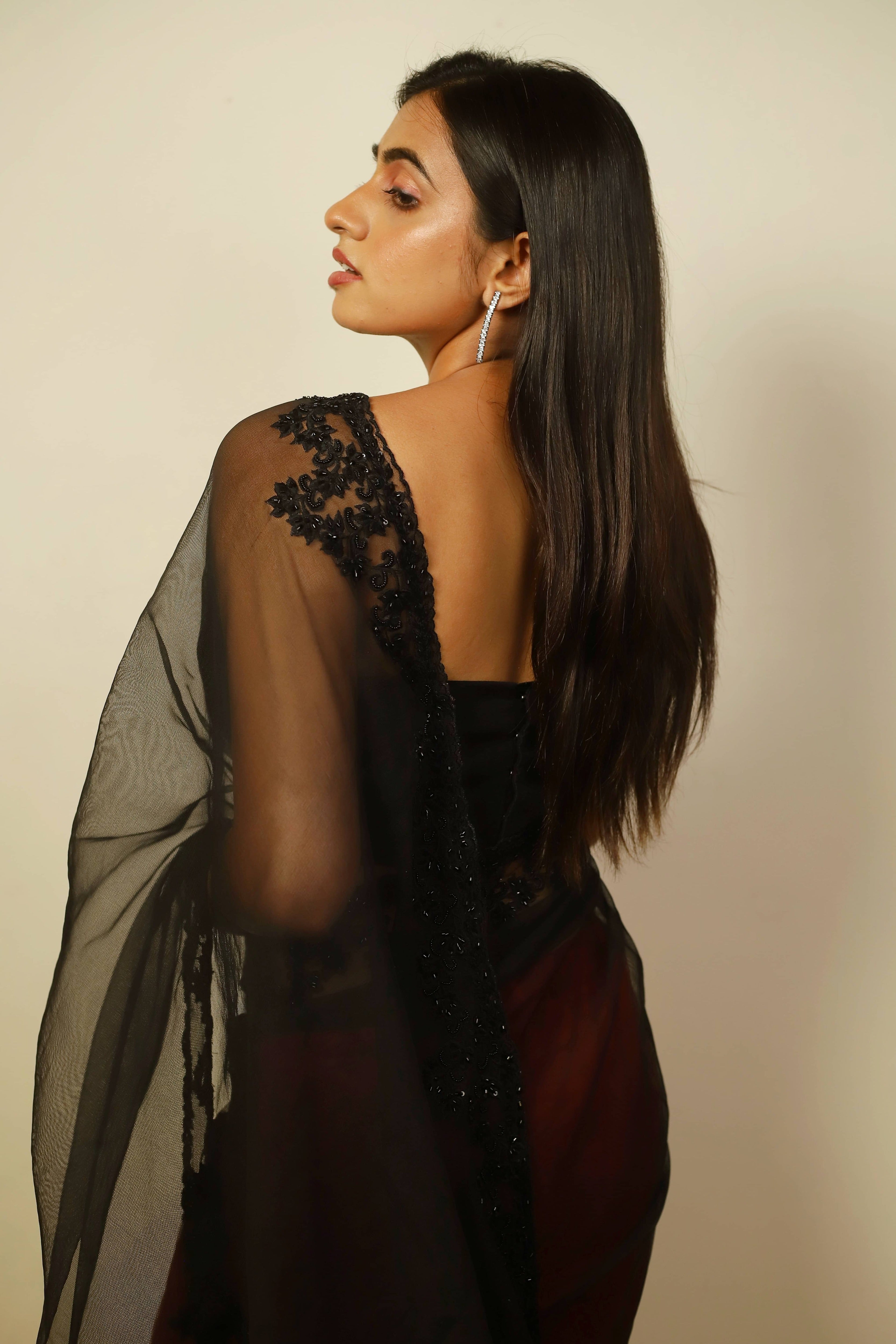 Actress Cherukuri Maanasa Choudhary who acted in the movie Lucky Baskhar with Dulquer Salmaan is seen in a red and black net saree with pallu and border detailings paired with a cut worked bralette with a plunge neck. Blouse back and saree border design.