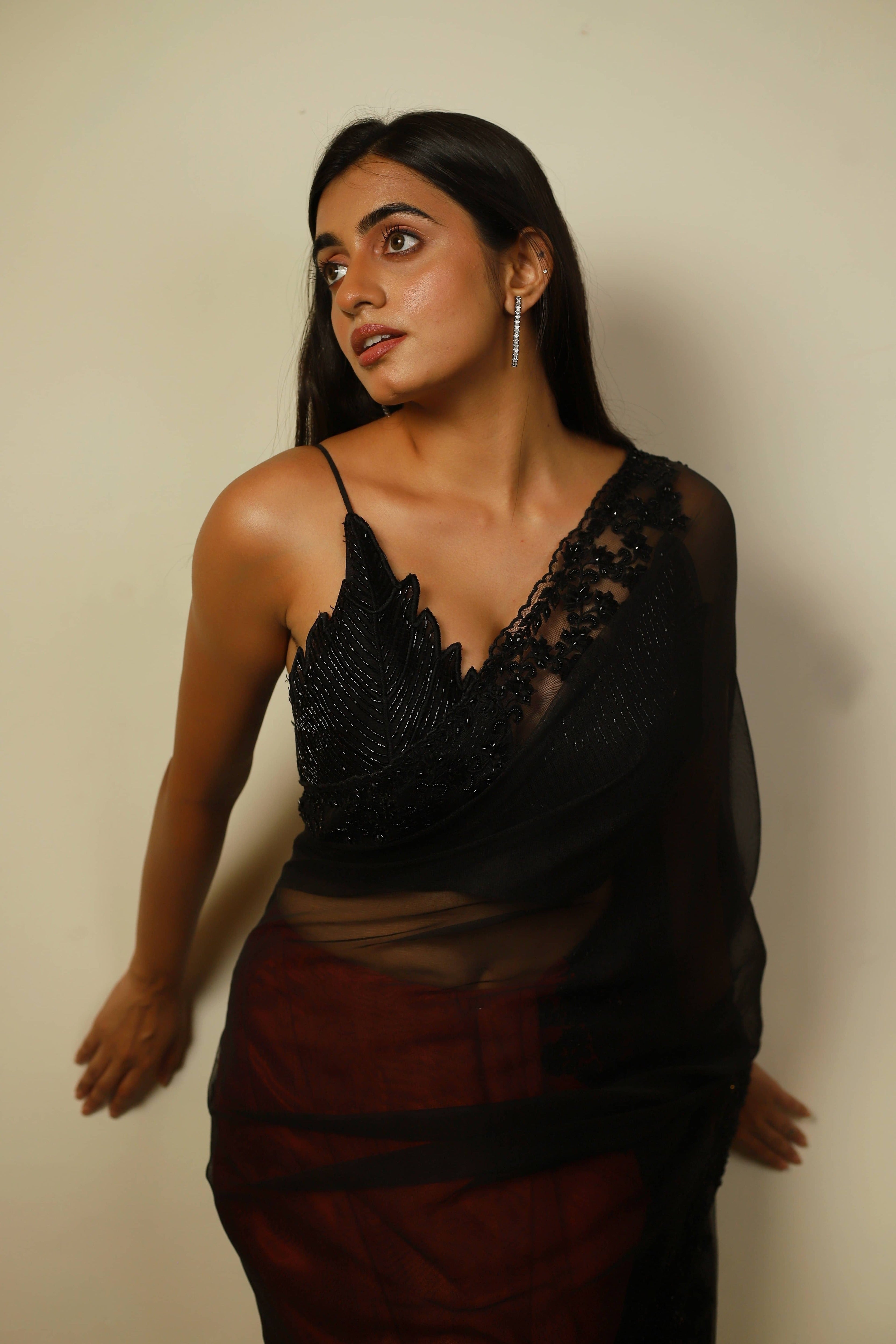 Actress Cherukuri Maanasa Choudhary who acted in the movie Lucky Baskhar with Dulquer Salmaan is seen in a red and black net saree with pallu and border detailings paired with a cut worked bralette with a plunge neck. Blouse detailing.