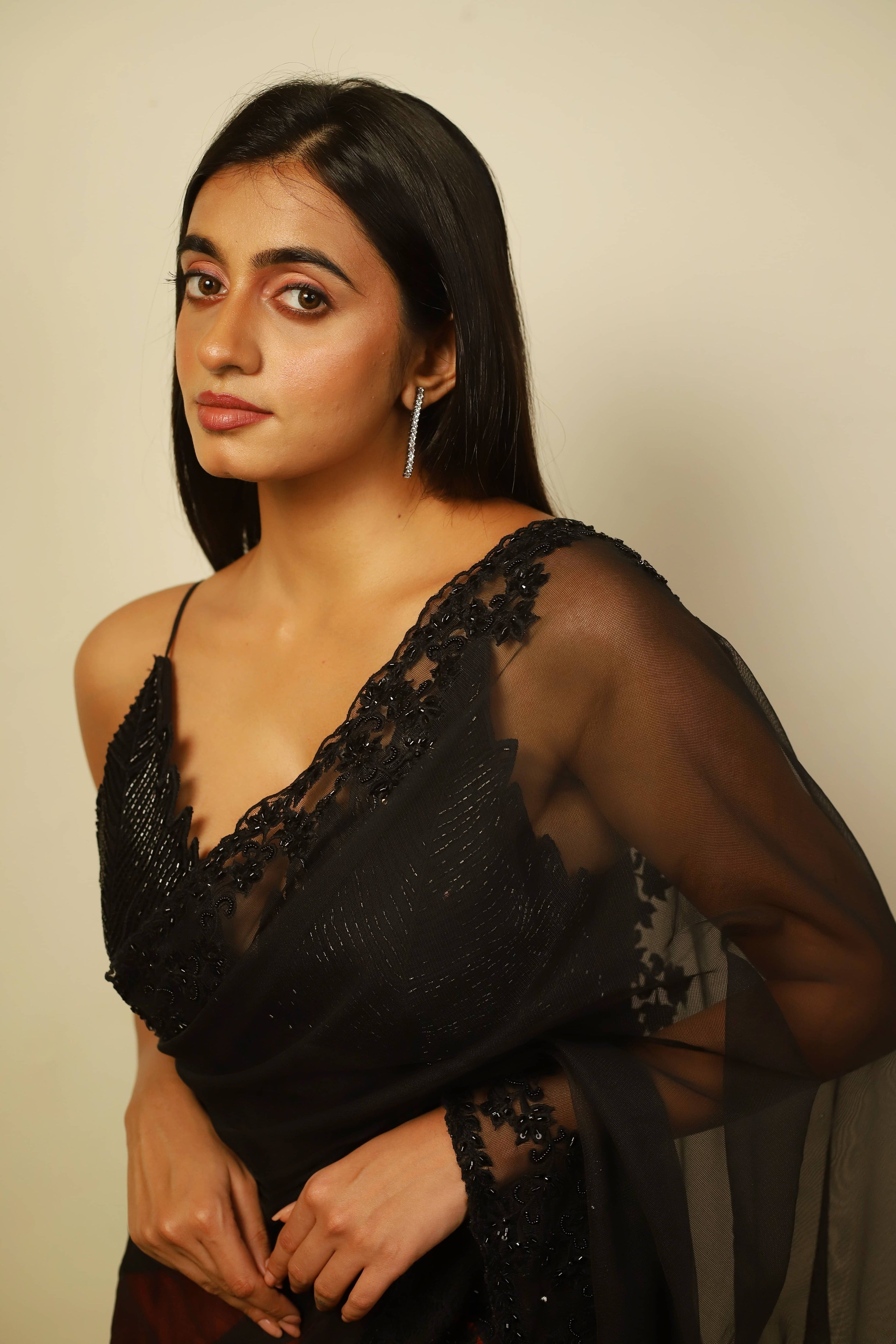Actress Cherukuri Maanasa Choudhary who acted in the movie Lucky Baskhar with Dulquer Salmaan is seen in a red and black net saree with pallu and border detailings paired with a cut worked bralette with a plunge neck. Full side blouse profile.