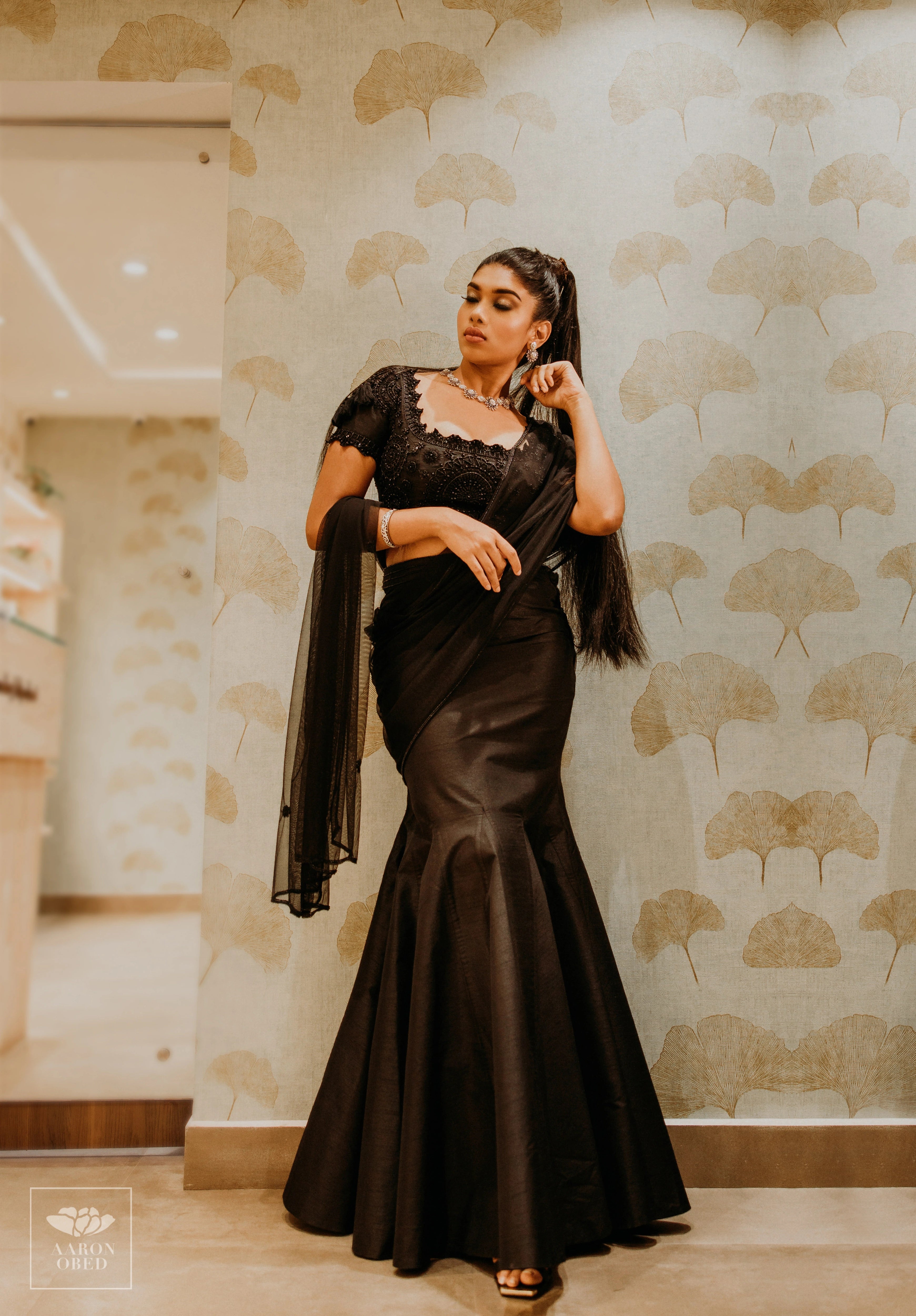 Actress Dushara Vijayan for a photoshoot in a black tulle and raw silk draped mermaid lehenga, intricately handcrafted with beads, sequins and resham by team Archana Karthick.