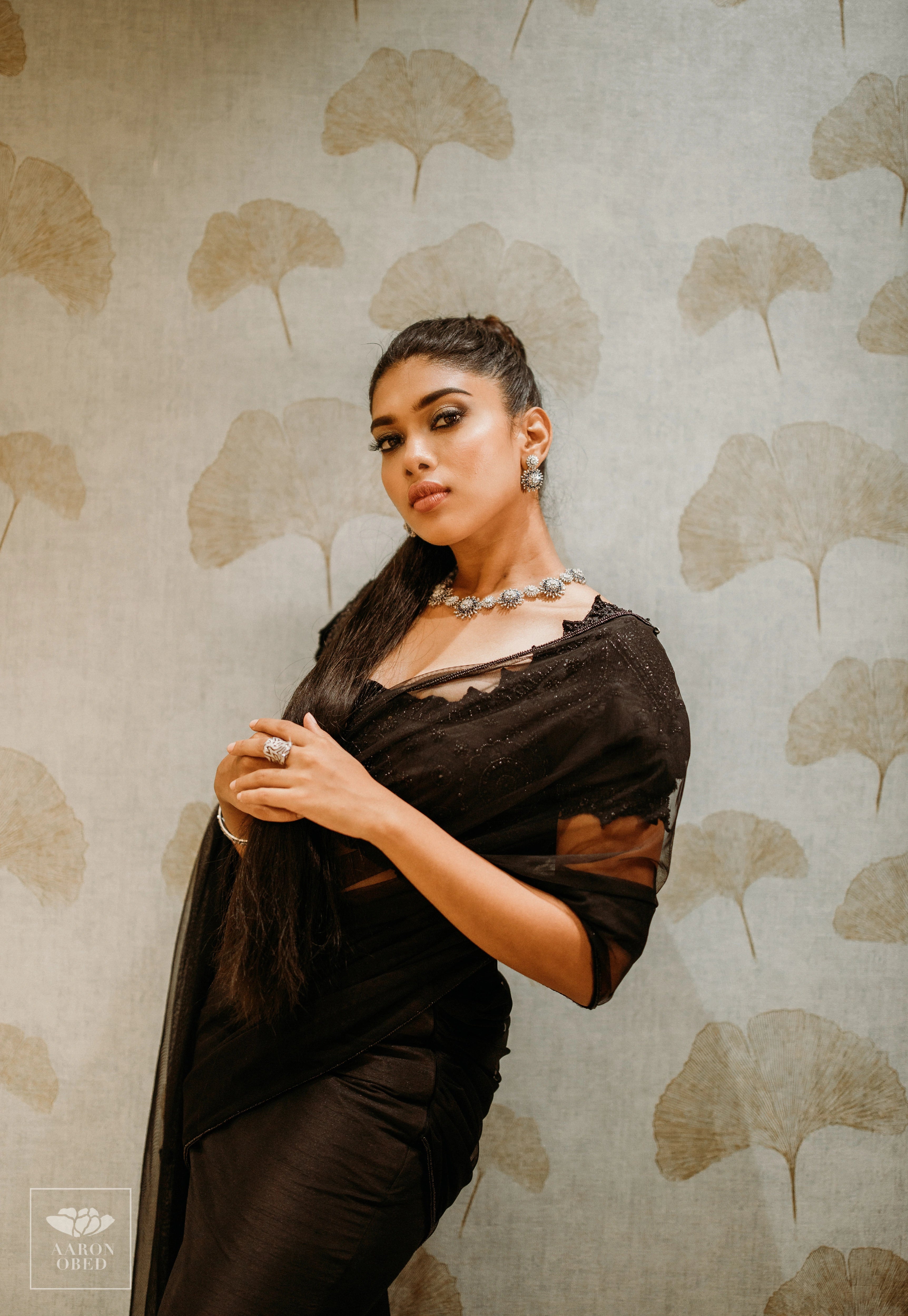 Actress Dushara Vijayan leaning in a black tulle and raw silk draped mermaid lehenga, intricately handcrafted with beads, sequins and resham by team Archana Karthick.