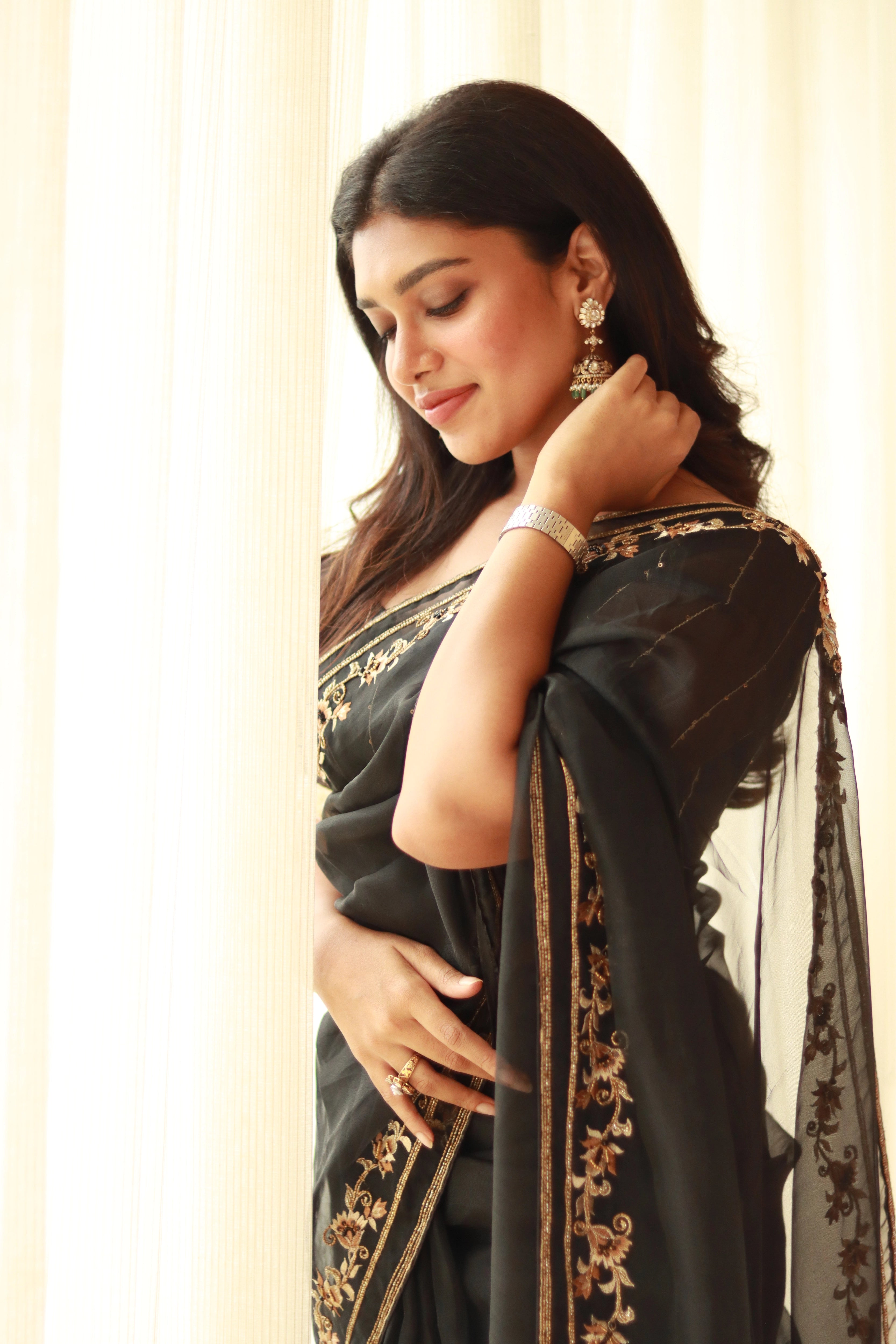 Actress Dushara Vijayan looking down in a black organza saree, intricately handcrafted with cutdana, zari, beads, sequins and resham by team Archana Karthick.