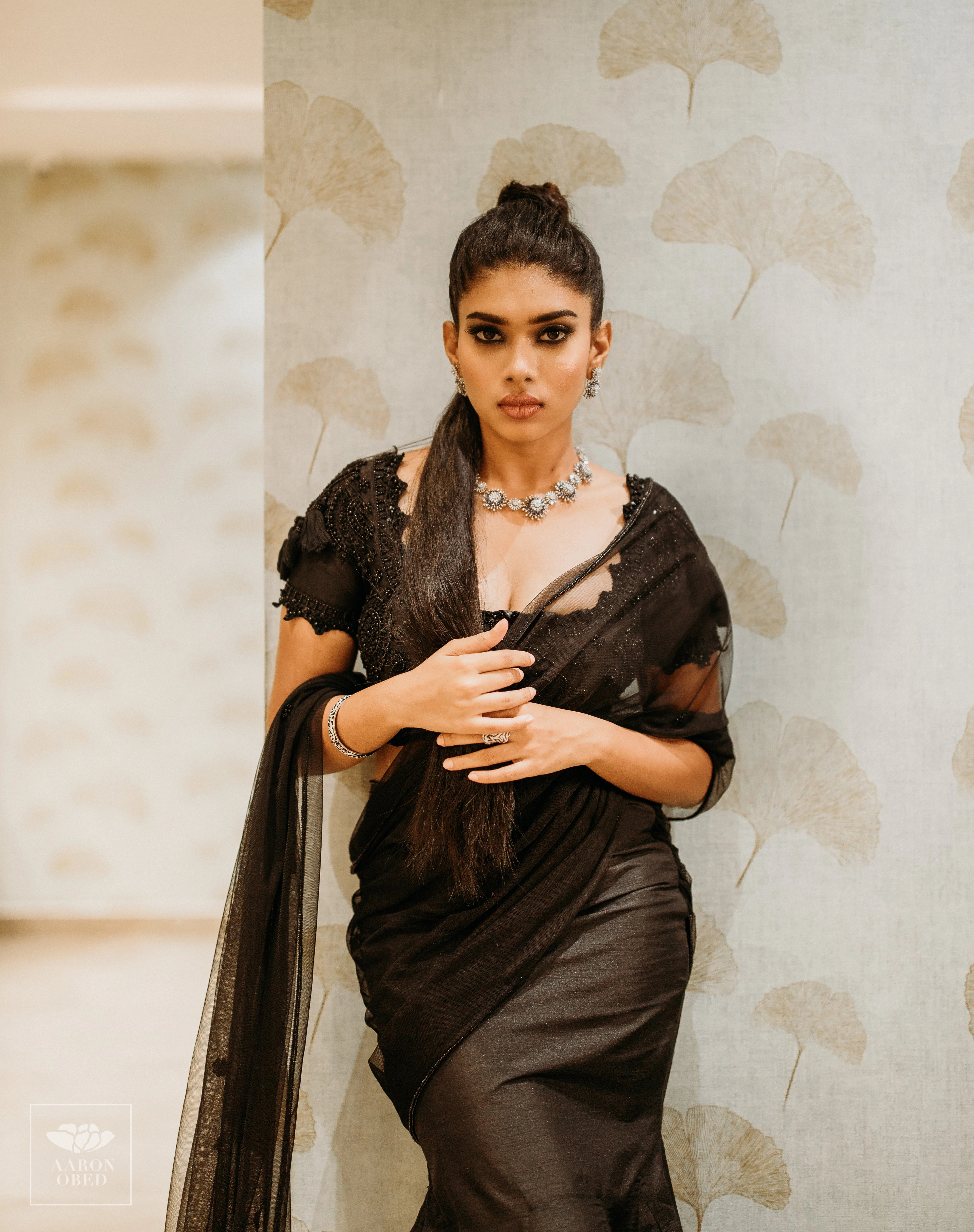 Actress Dushara Vijayan looking straight at the lens in a black tulle and raw silk draped mermaid lehenga, intricately handcrafted with beads, sequins and resham by team Archana Karthick.