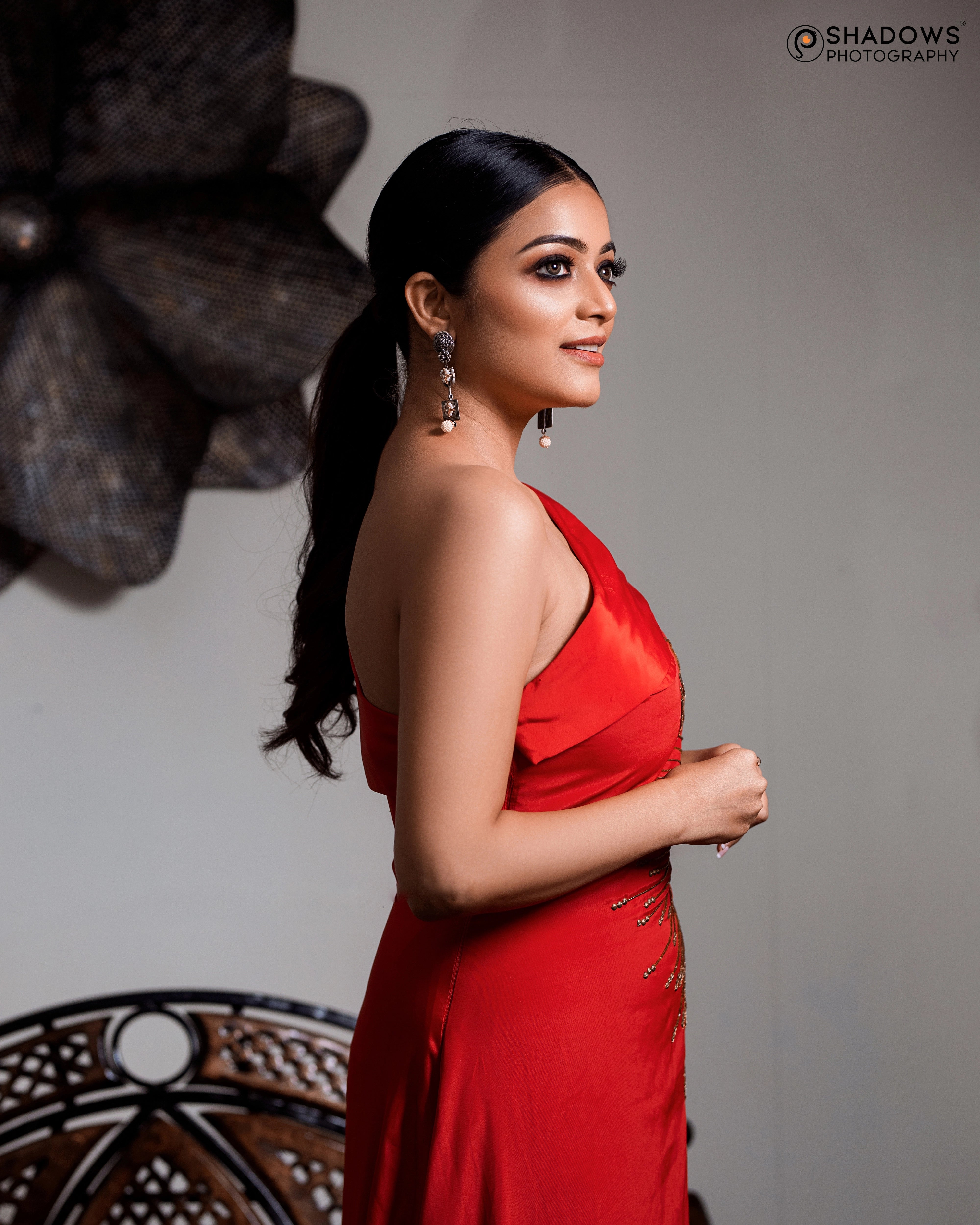 Actress Janai Iyer posing for side profile in a red crepe silk one-shoulder asymmetric gown, intricately handcrafted with sequins, zardozi, cutdana and beads by team Archana Karthick.