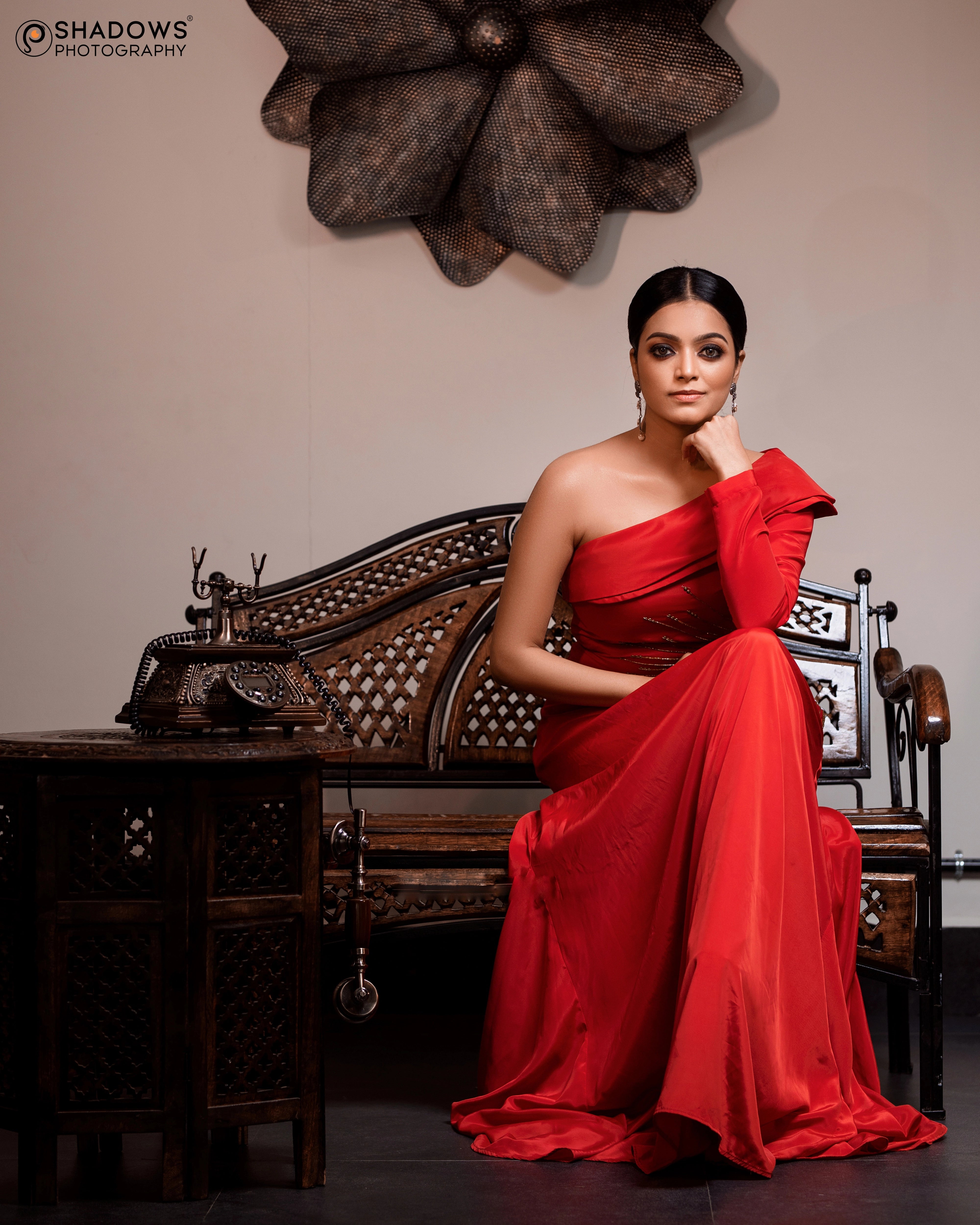 Actress Janai Iyer seated in a red crepe silk one-shoulder asymmetric gown, intricately handcrafted with sequins, zardozi, cutdana and beads by team Archana Karthick.