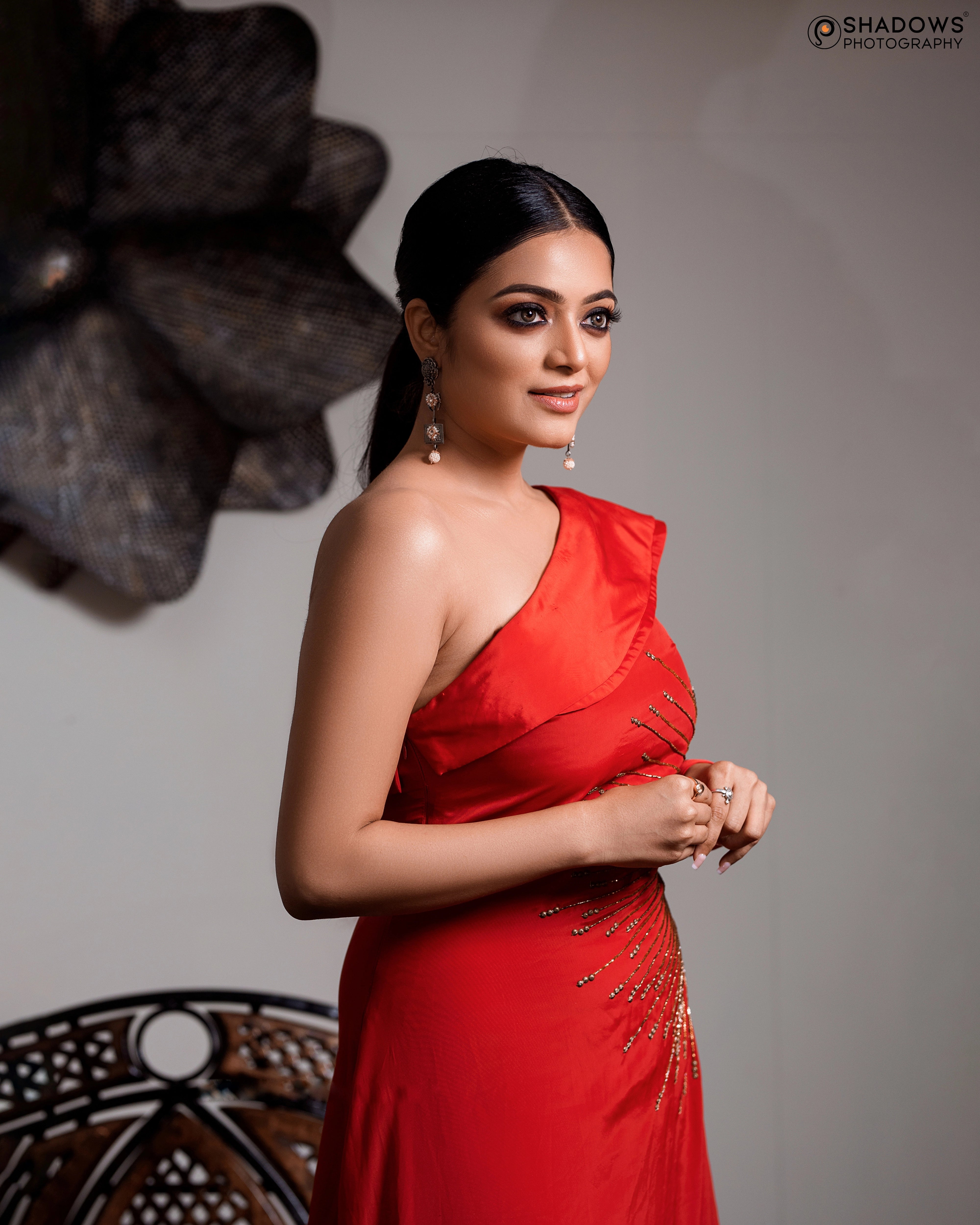 Actress Janai Iyer smiling in a red crepe silk one-shoulder asymmetric gown, intricately handcrafted with sequins, zardozi, cutdana and beads by team Archana Karthick.
