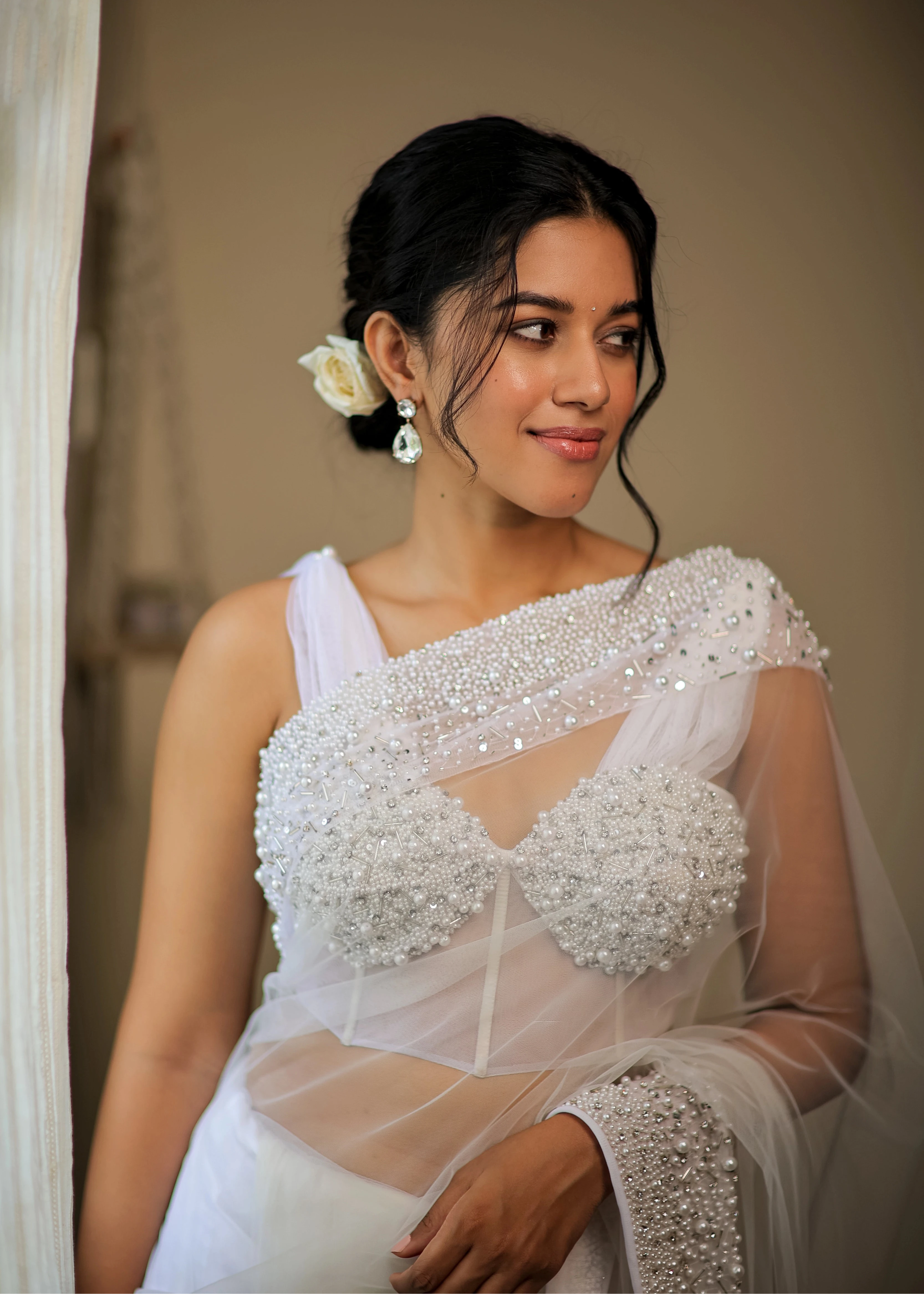Actress Mirnalini Ravi smiling in a pearl white saree intricately embellished with pearls and cut beads, paired with an off-shoulder corset with cowl sleeves.