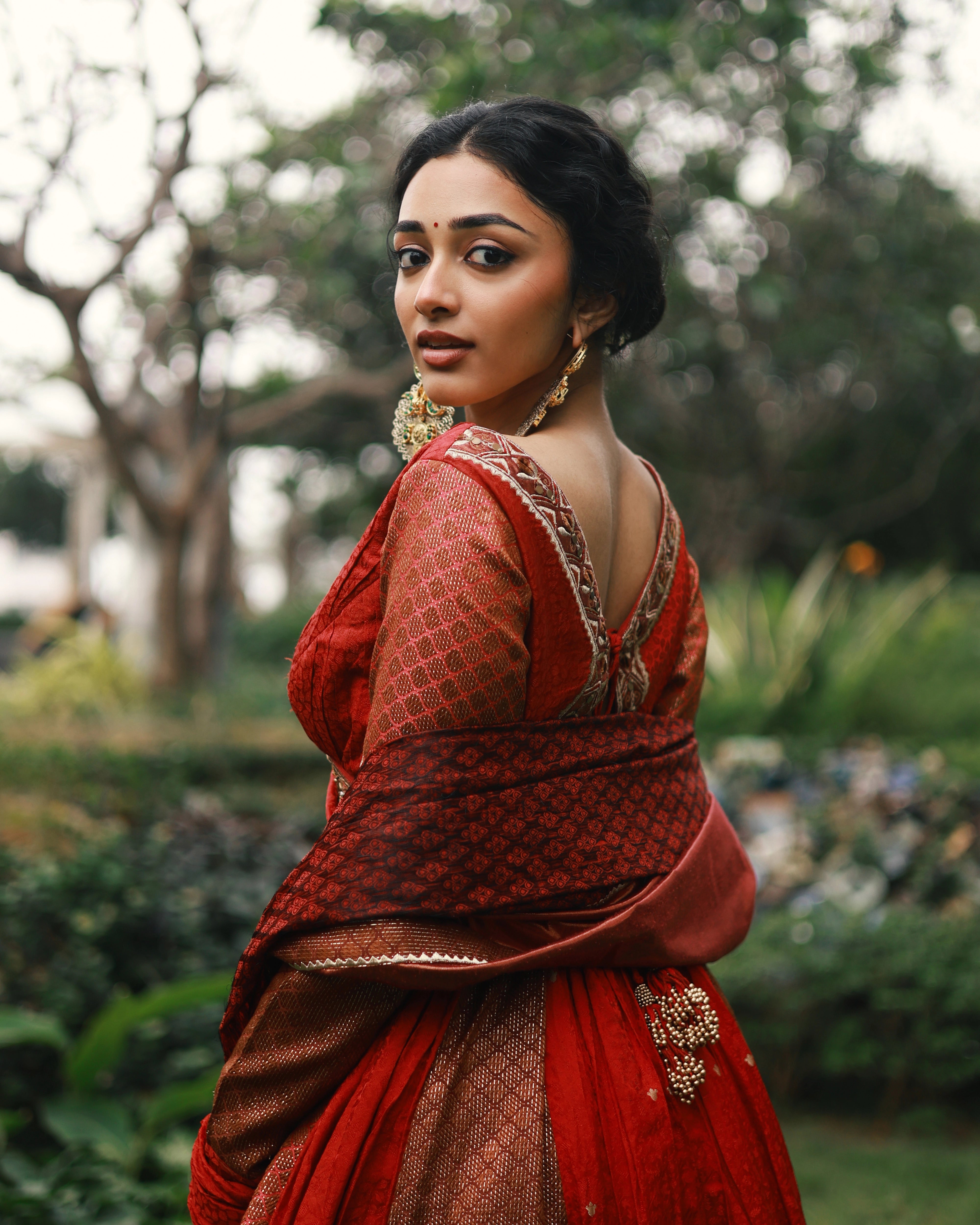 Actress Preity Mukhundhan posing in a red-orange banarasi tissue and silk angrakha anarkali with a sharara pant and tissue dupatta by team Archana Karthick.