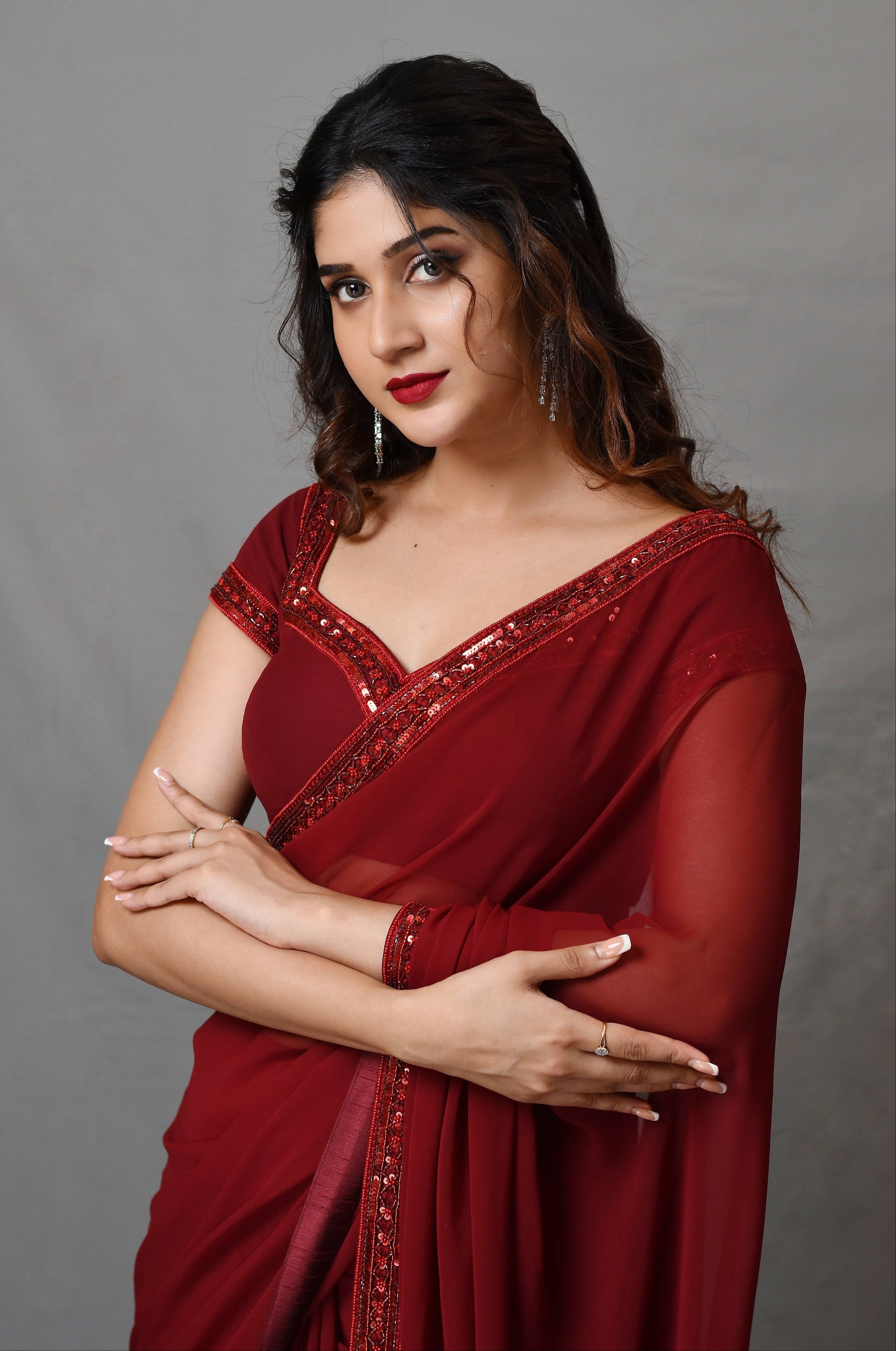 Actress Rabiya Khatoon in a ruby red georgette saree set designed by Archana Karthick. half front profile.