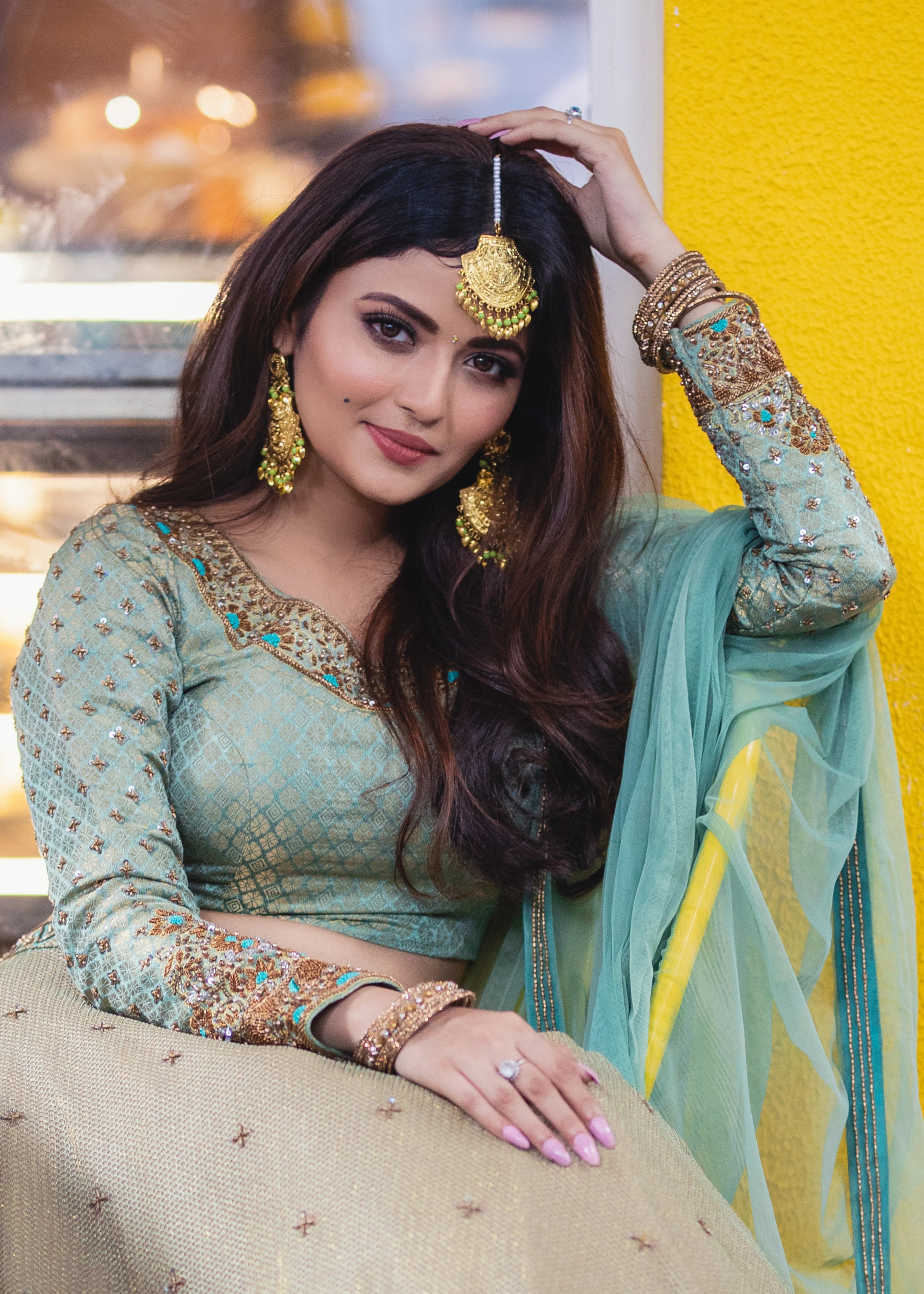 Actress Shirin Kanchwala in a handcrafted banaras (brocade) lehenga in shades of light sea green / pista blue / cyan designed by Archana Karthick smiling at the camera with hand on her hair