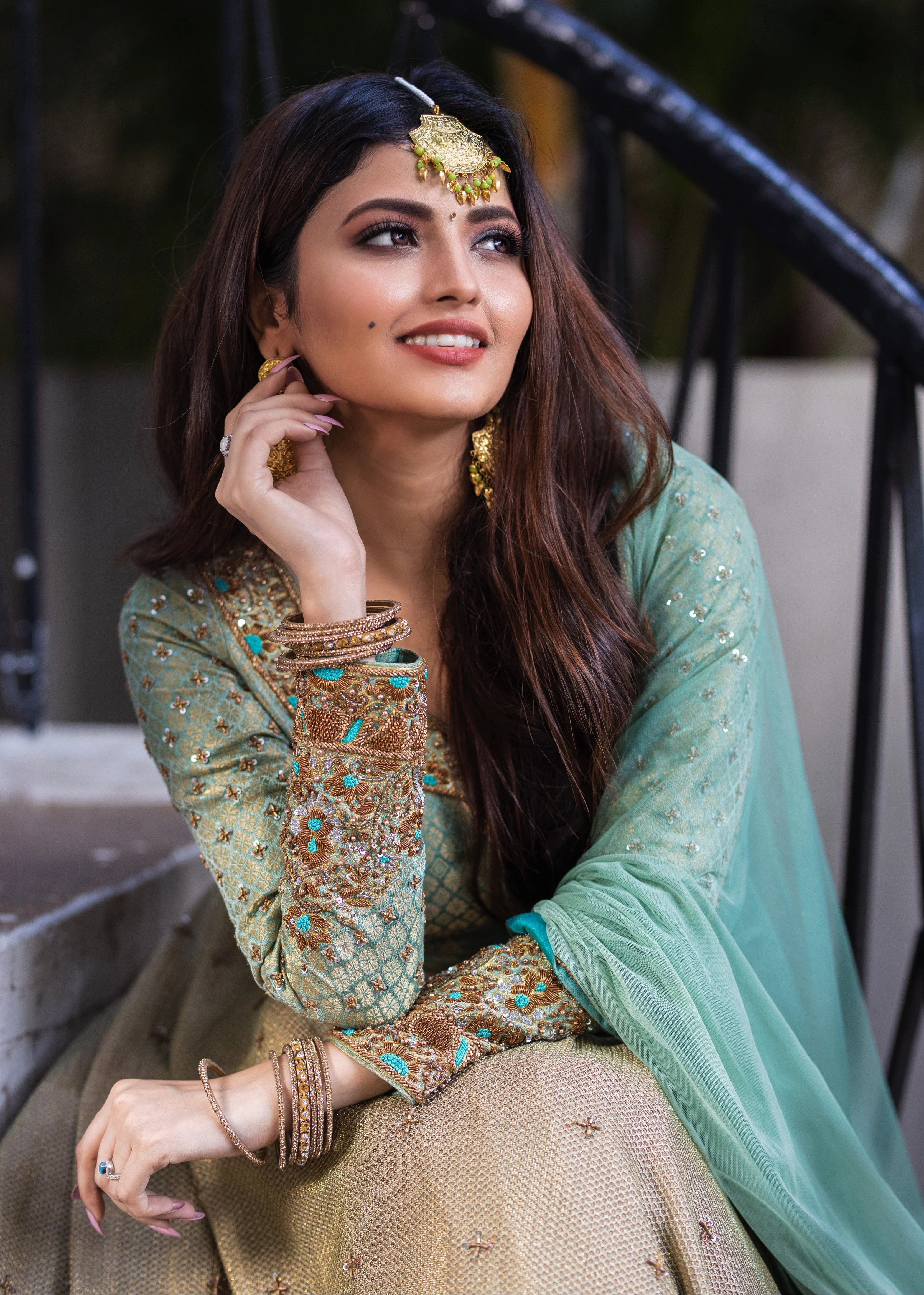 Actress Shirin Kanchwala in a handcrafted banaras (brocade) lehenga in shades of light sea green / pista blue / cyan designed by Archana Karthick smiling with hand on earring