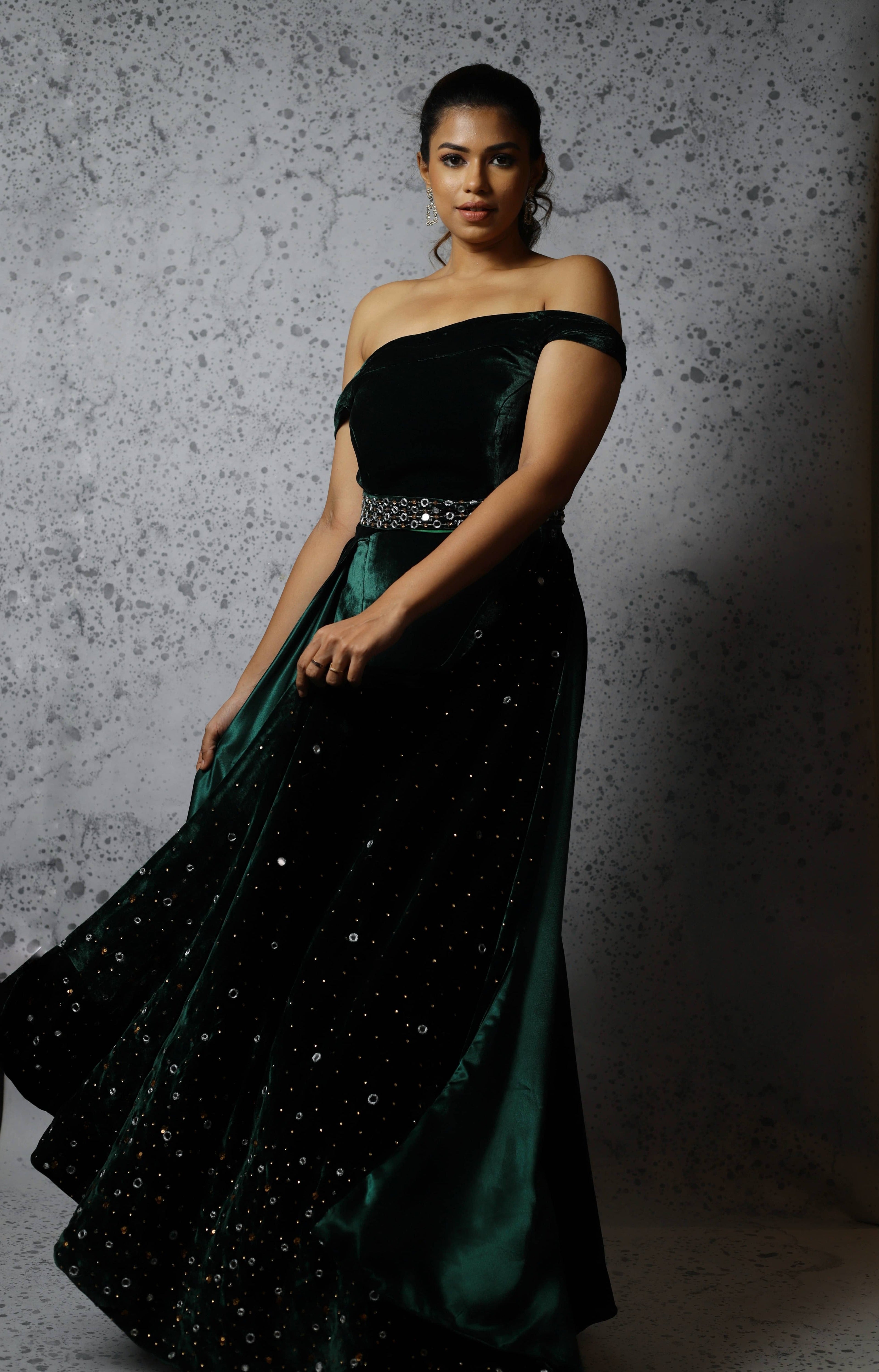 Actress Shrisha the niece of superstar actress Sridevi in a green velvet mermaid gown dress with detachable embellished belt and side trail. Front profile mid twirl picture.
