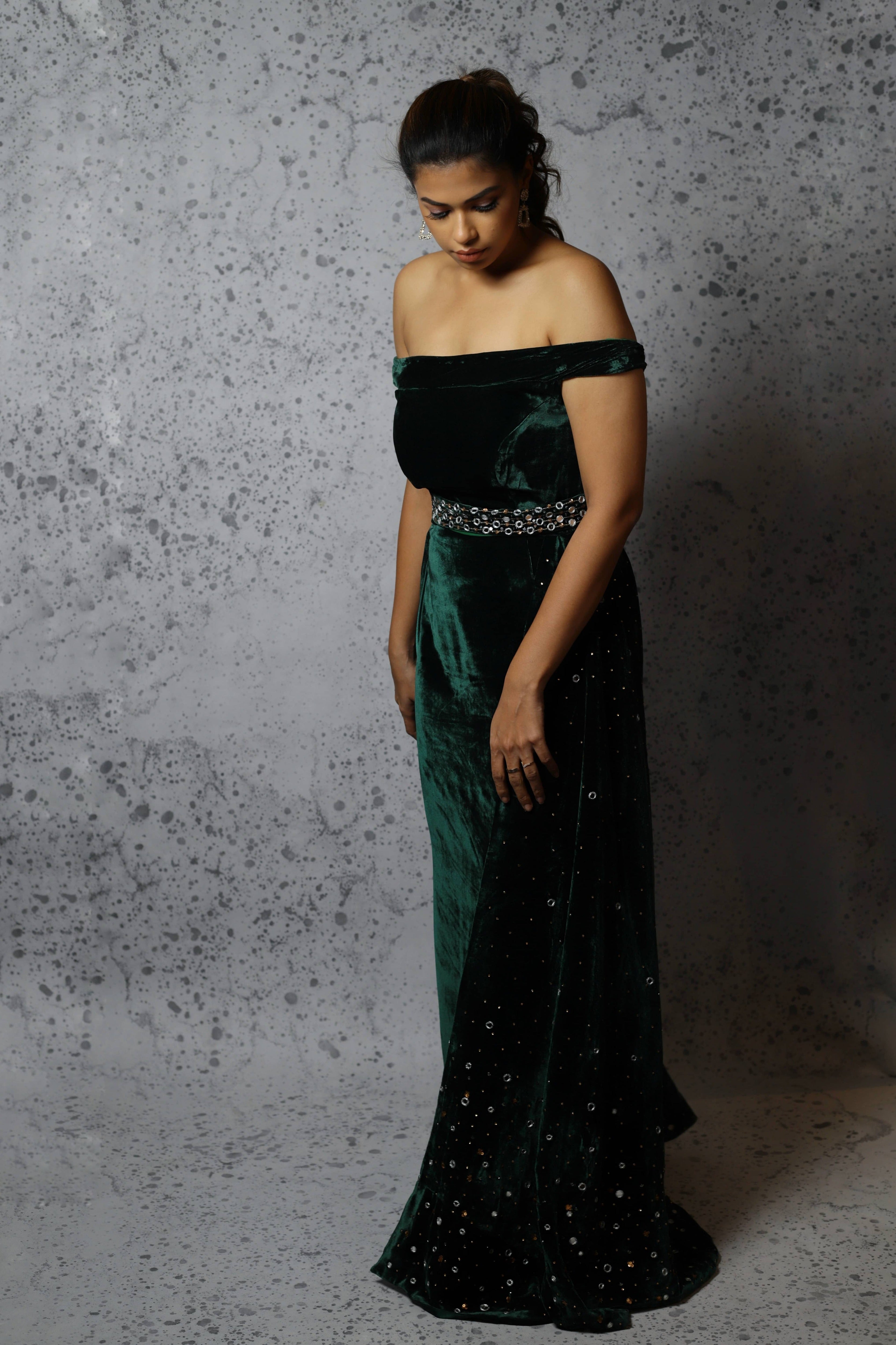 Actress Shrisha the niece of superstar actress Sridevi in a green velvet mermaid gown dress with detachable embellished belt and side trail. Full front profile looking down