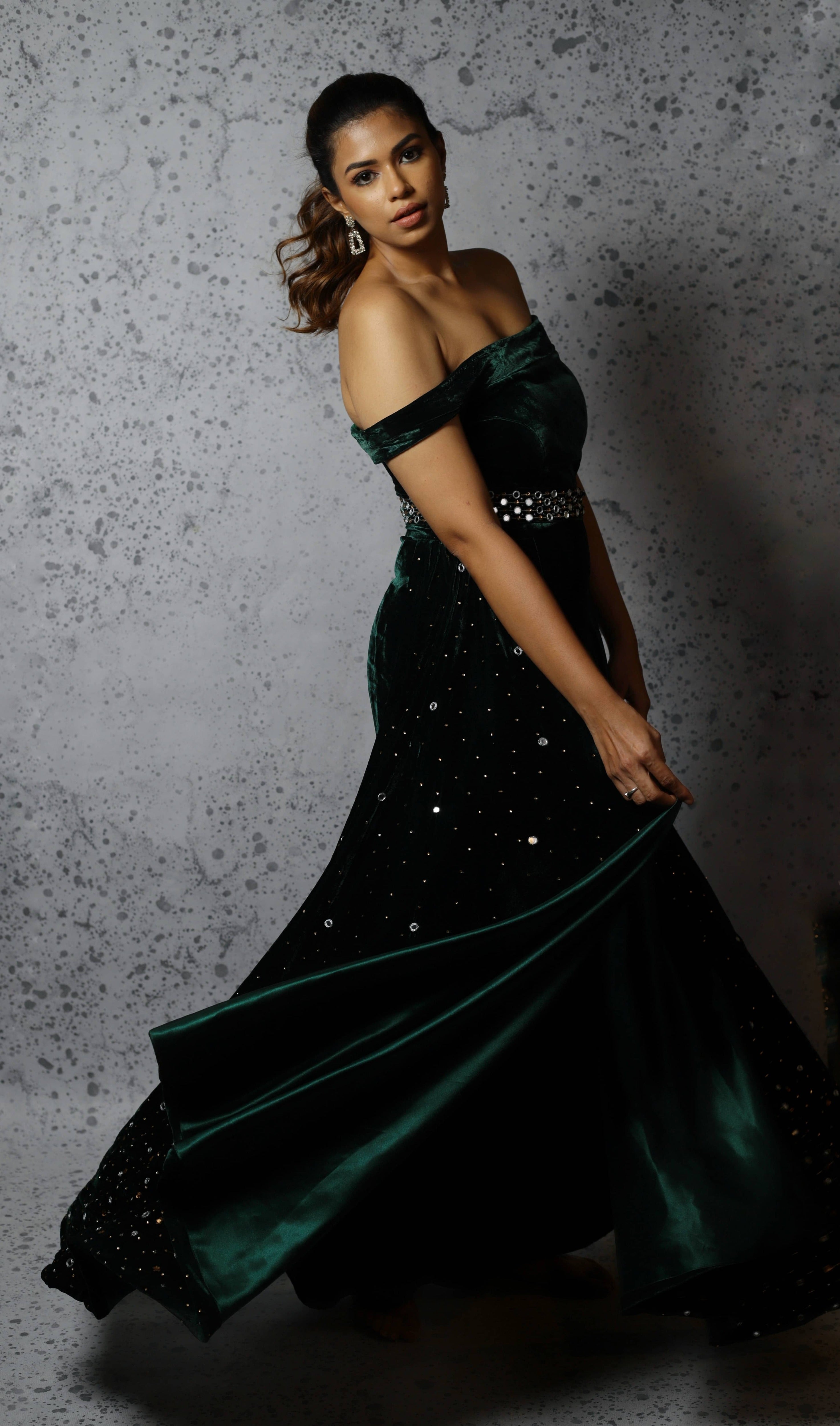 Actress Shrisha the niece of superstar actress Sridevi in a green velvet mermaid gown dress with detachable embellished belt and side trail. Side profile mid twirl picture.