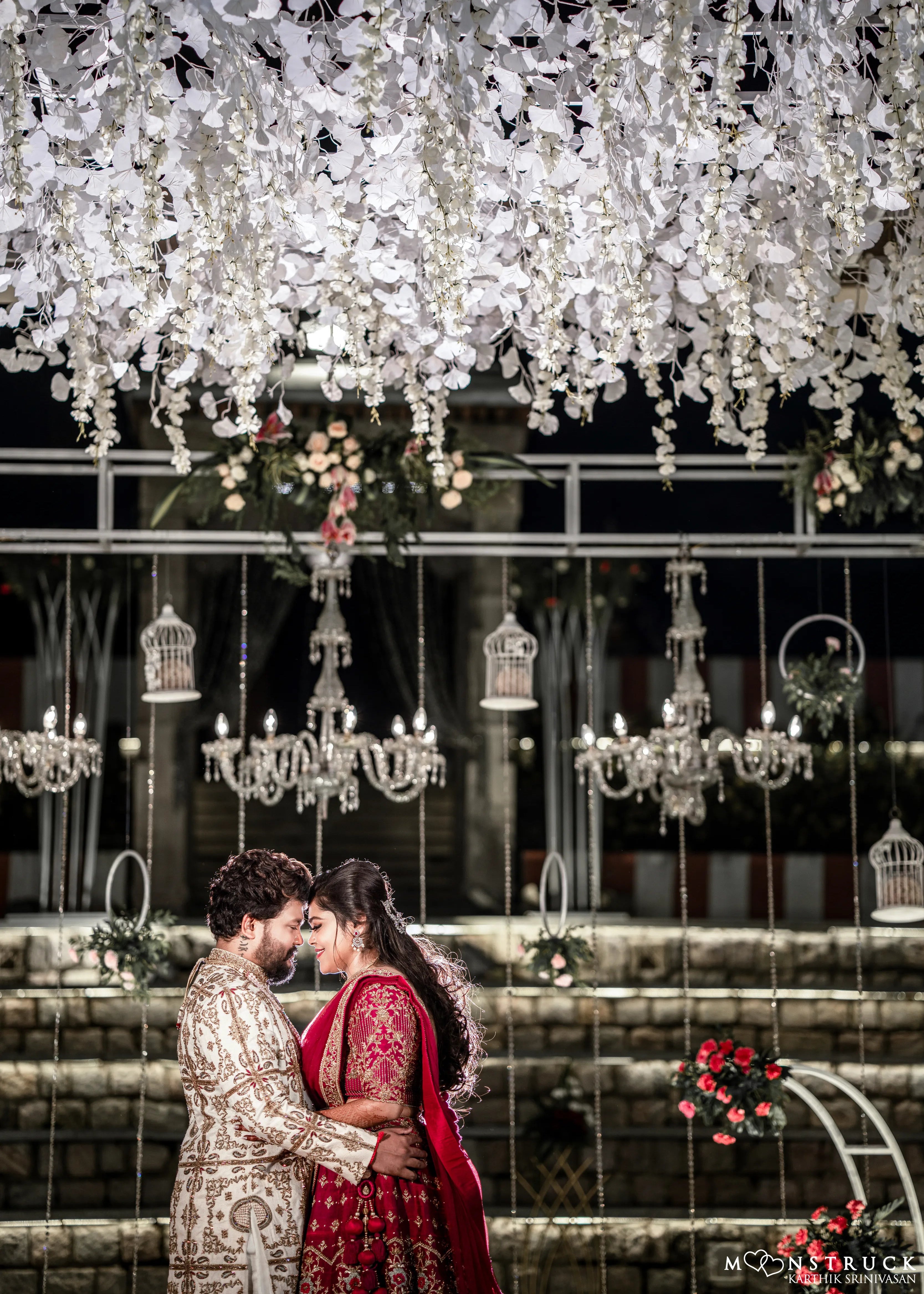 Anjana (Coimbatore) and Sandeep (Chennai) in an embrace in custom Archana Karthick for their wedding. Bridal lehenga is a magenta red raw silk with zardozi and resham knot work embellishments. Grrom's sherwani has similar work on ivory raw silk. The picture has beautiful crystal chandeliers in the background.