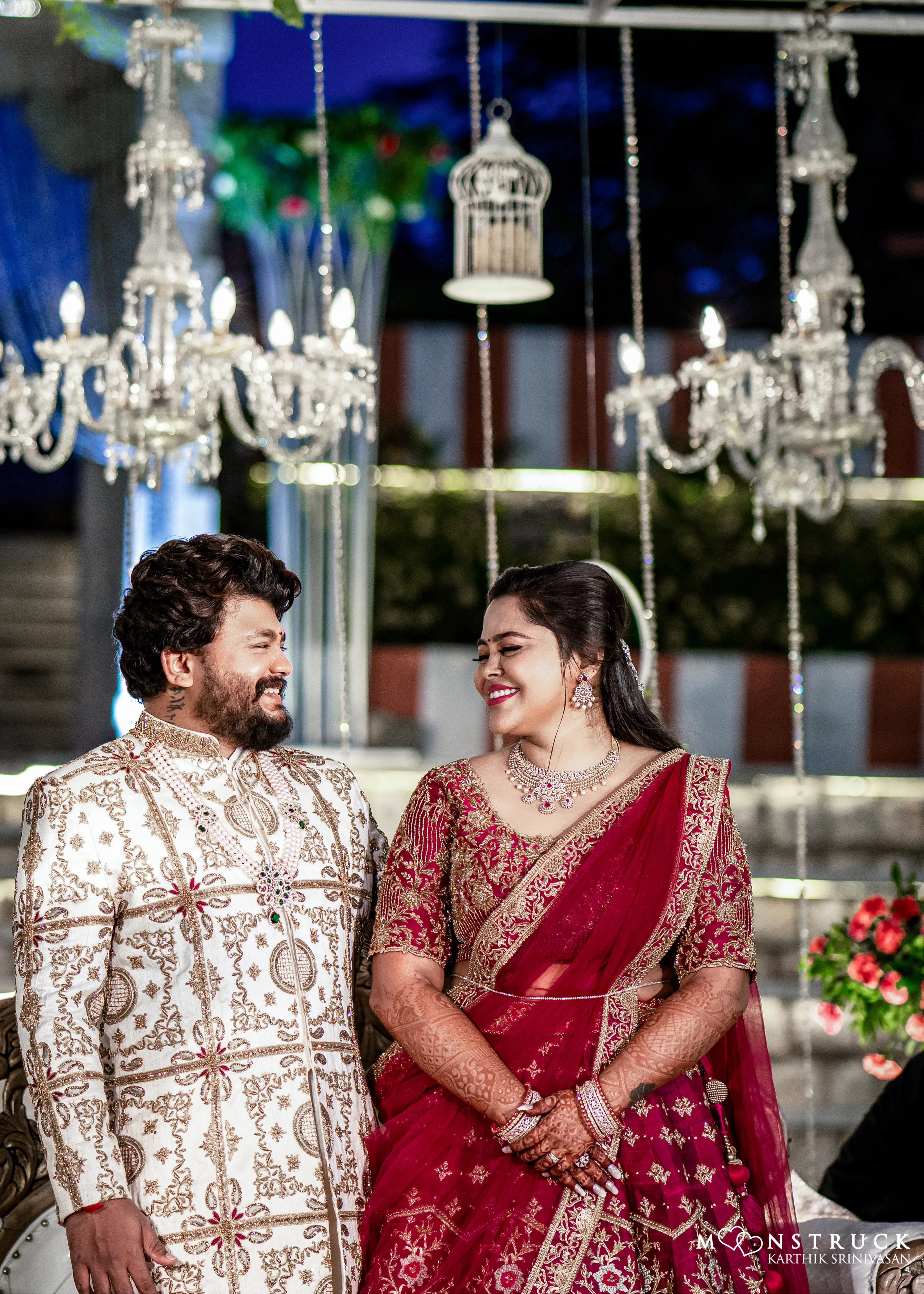 Anjana (Coimbatore) and Sandeep (Chennai) smiling in custom Archana Karthick for their wedding. Bridal lehenga is a magenta red raw silk with zardozi and resham knot work embellishments. Grrom's sherwani has similar work on ivory raw silk.