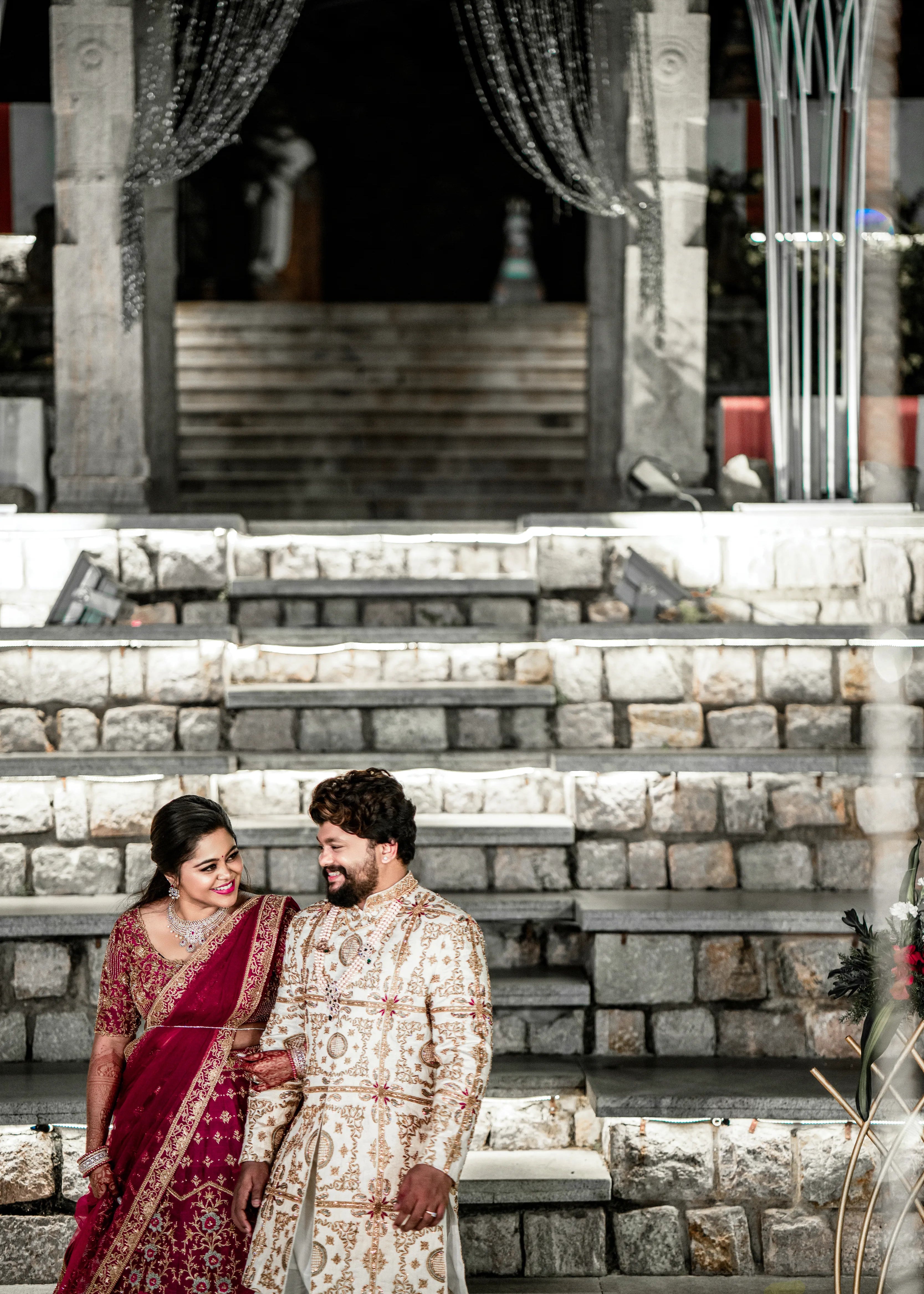 Anjana (Coimbatore) and Sandeep (Chennai) walking hand in hand in custom Archana Karthick for their wedding. Bridal lehenga is a magenta red raw silk with zardozi and resham knot work embellishments. Grrom's sherwani has similar work on ivory raw silk.