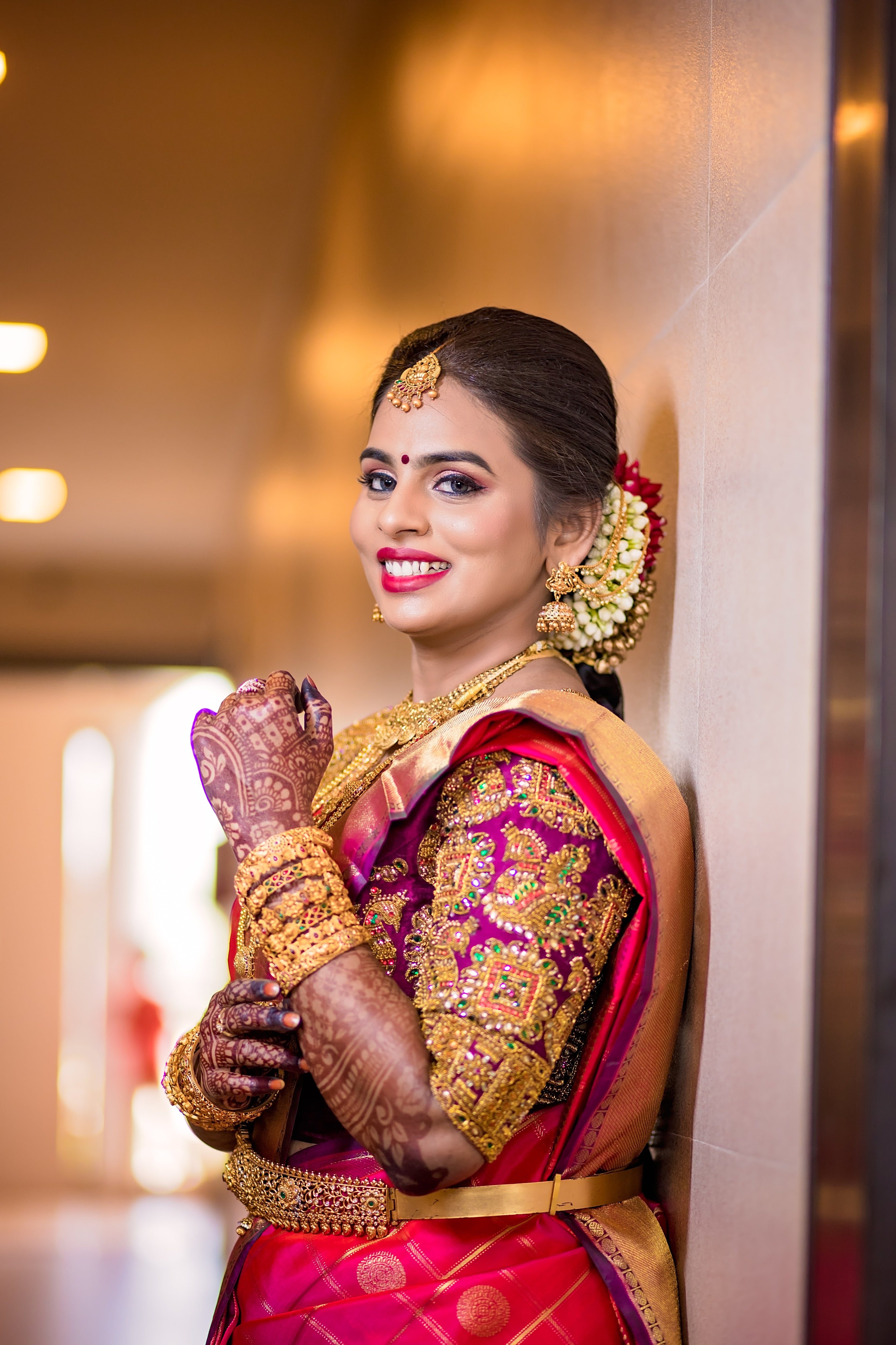 Archana Karthick Bride Kowsalya in a concept bridal blouse in purple raw silk. The blouse is heavily embellished with zardozi, kemp stones, beads and is half or elbow sleeved. The bride is posing with her left arm bent at the elbowhighlighting the left sleeve.