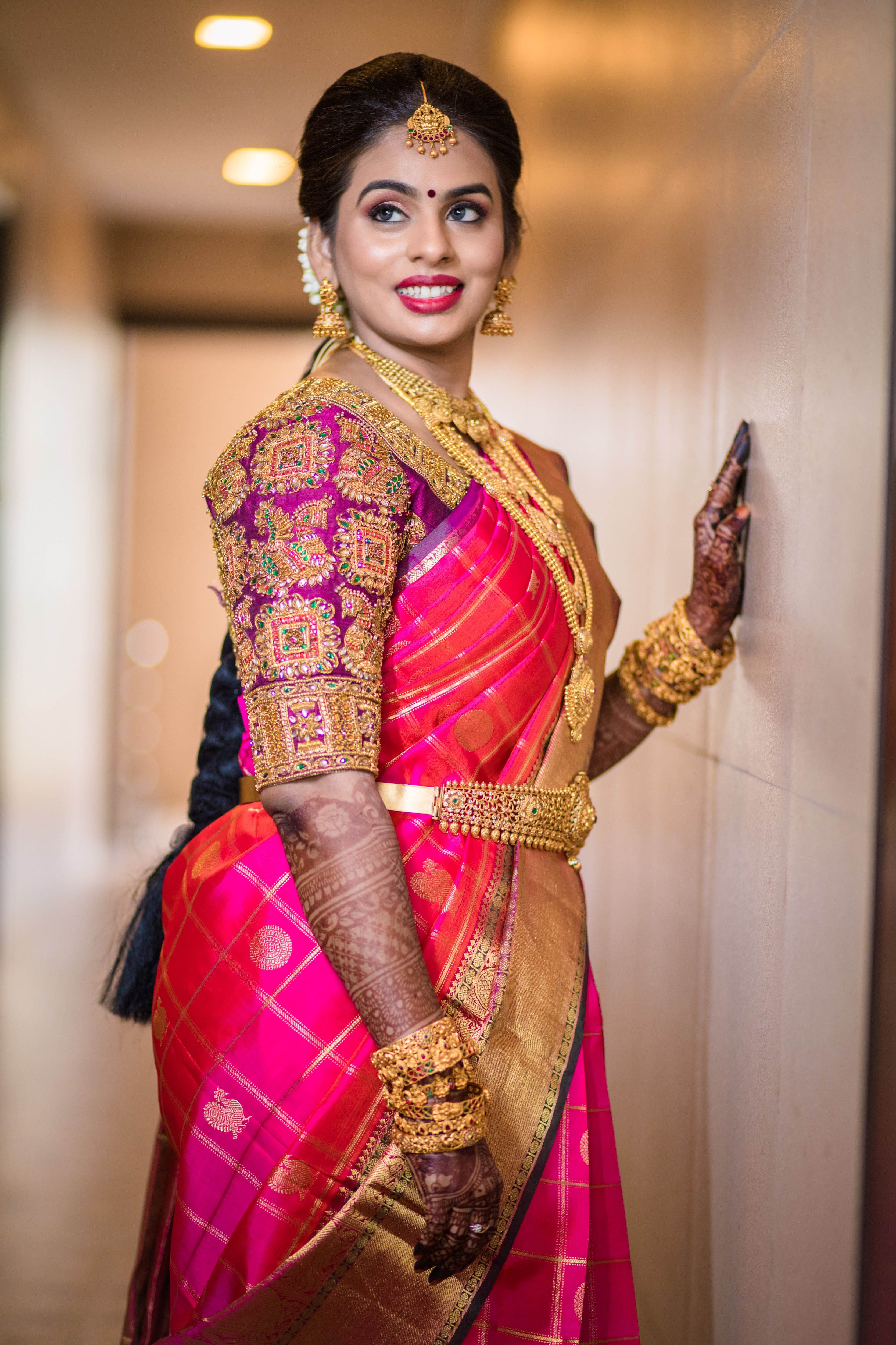 Archana Karthick Bride Kowsalya in a concept bridal blouse in purple raw silk. The blouse is heavily embellished with zardozi, kemp stones, beads and is half or elbow sleeved. The bride is posing with a smile looking to her right.