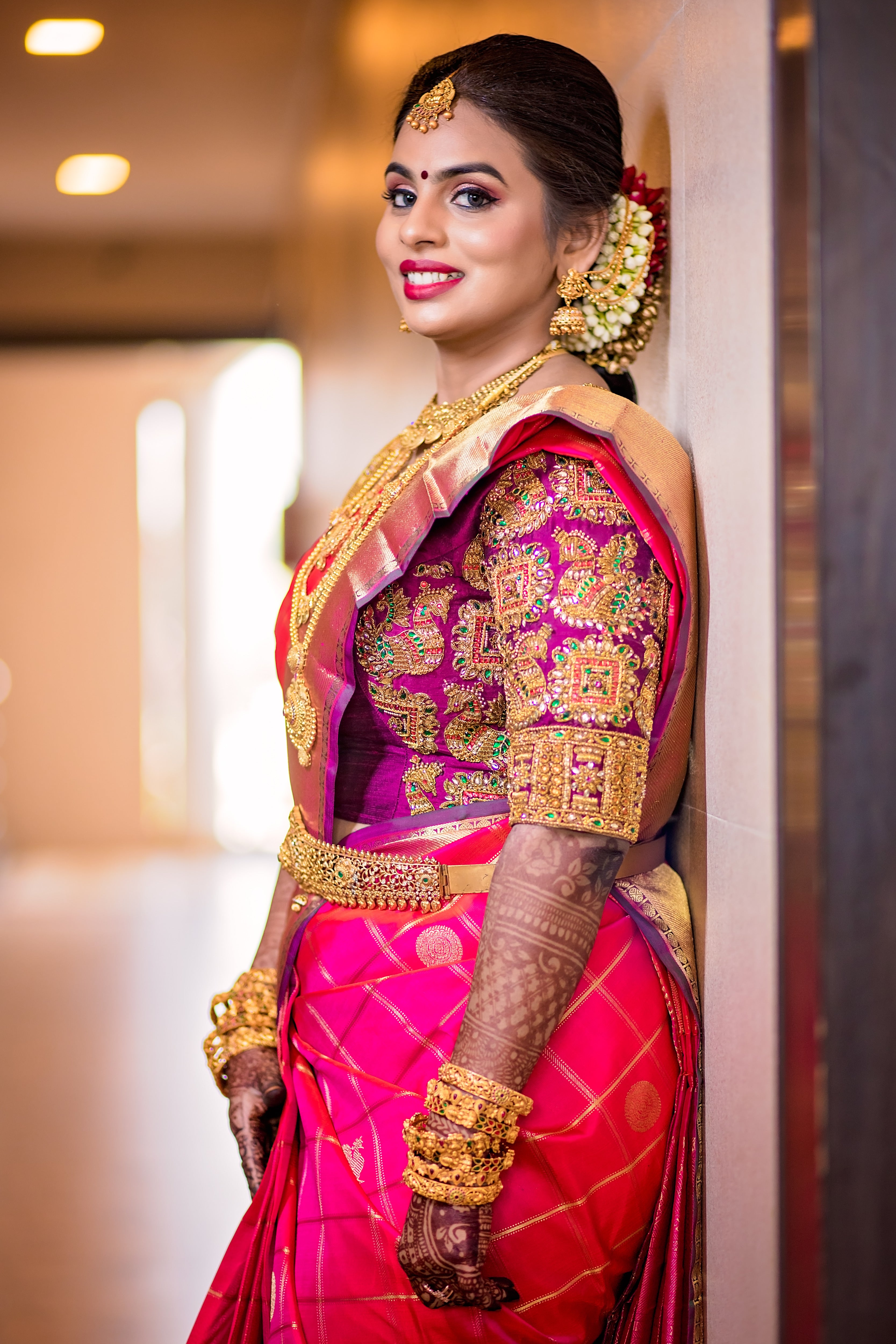 Archana Karthick Bride Kowsalya in a concept bridal blouse in purple raw silk. The blouse is heavily embellished with zardozi, kemp stones, beads and is half or elbow sleeved. The bride is posing with a smile looking to her left.