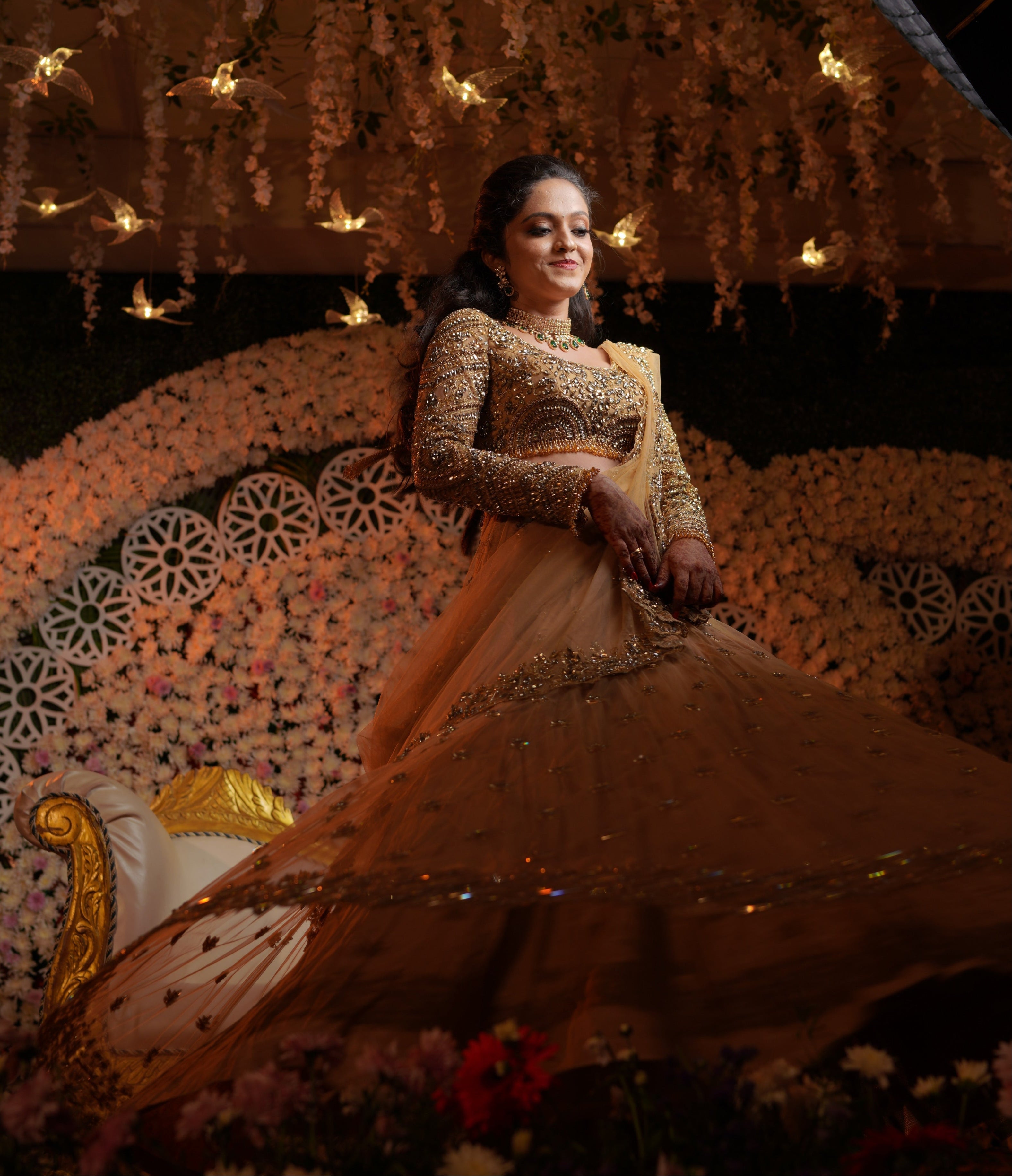 Archana Karthick Bride Shravanthi Karade golden beige lehenga with stonework twirls on stage with a smile. The outfit has cutworked borders or seams of the dupatta (veil) and of the skirt. The seams of the blouse are embellished with crystal drops or stones. The mandala motifs on the blouse look stunning with rhinestone work, crystals and cut dana work.