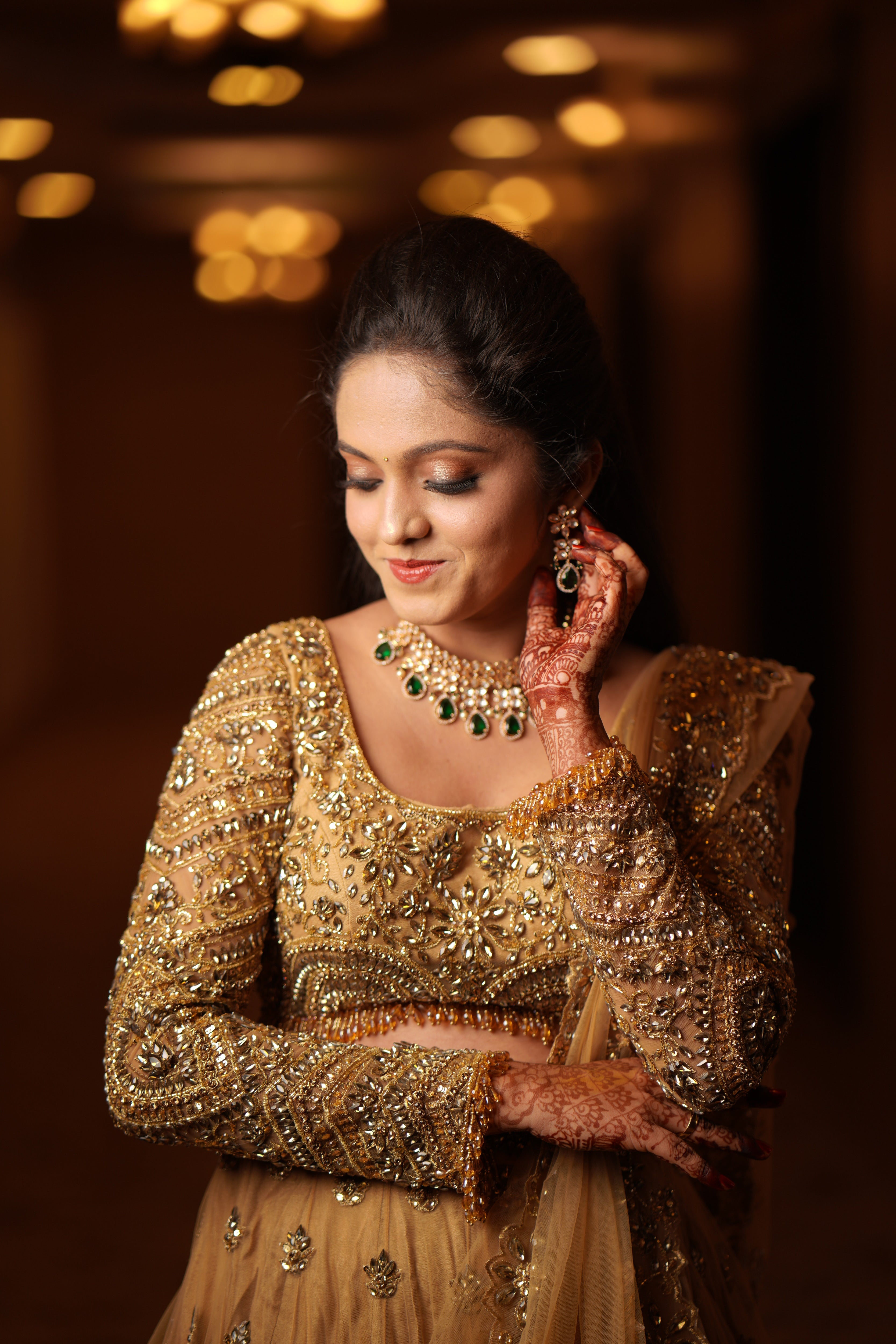 Archana Karthick Bride in golden beige lehenga with stonework poses for a front profile photo covering only the front of the blouse.The outfit has cutworked borders or seams of the dupatta (veil) and of the skirt. The seams of the blouse are embellished with crystal drops or stones. The mandala motifs on the blouse look stunning with rhinestone work, crystals and cut dana work.