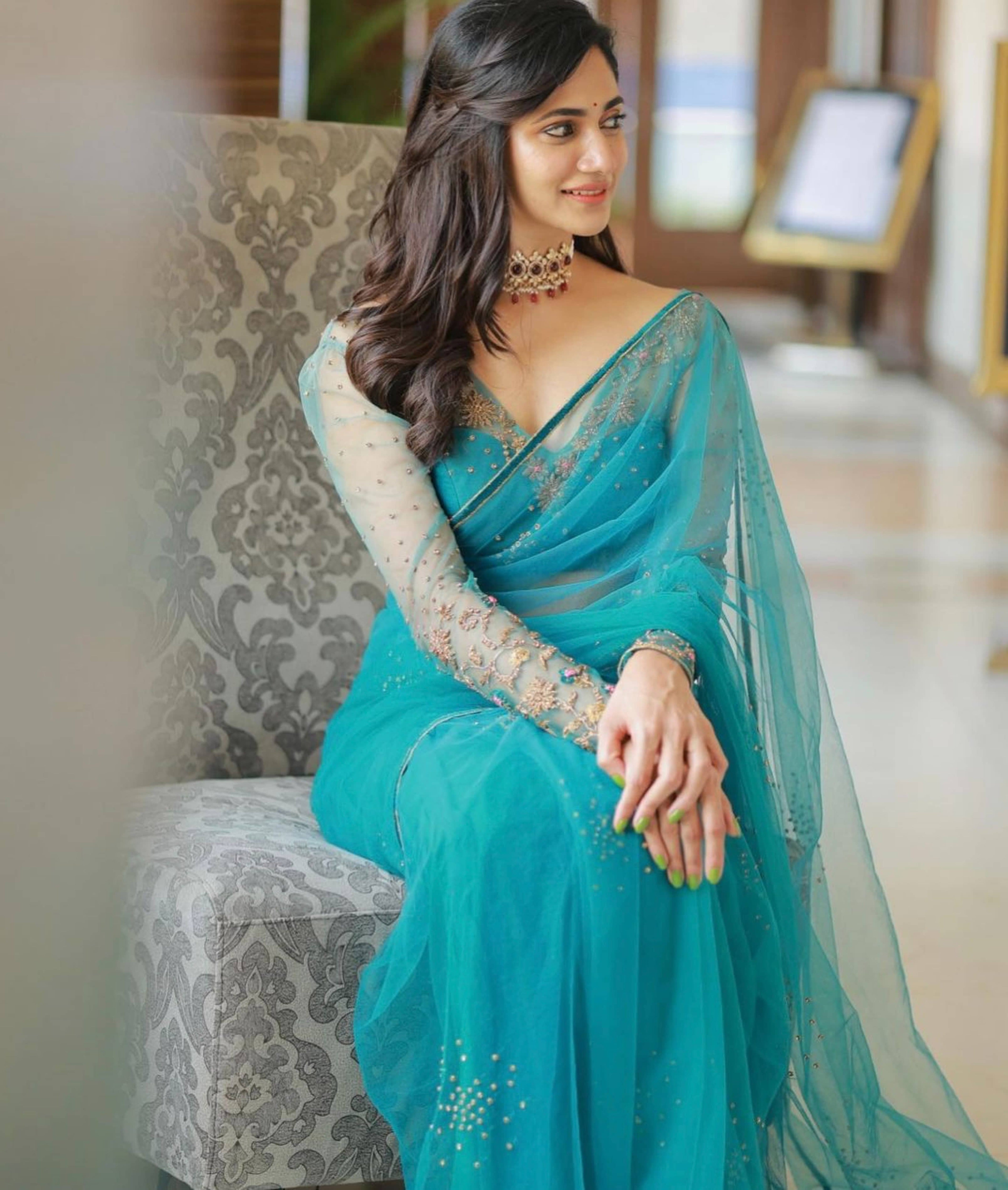 Bigg Boss fame and actress Losliya Mariyanesan in a teal blue handcrafted saree set designed by Archana Karthick. Looking away from the camera and seated.