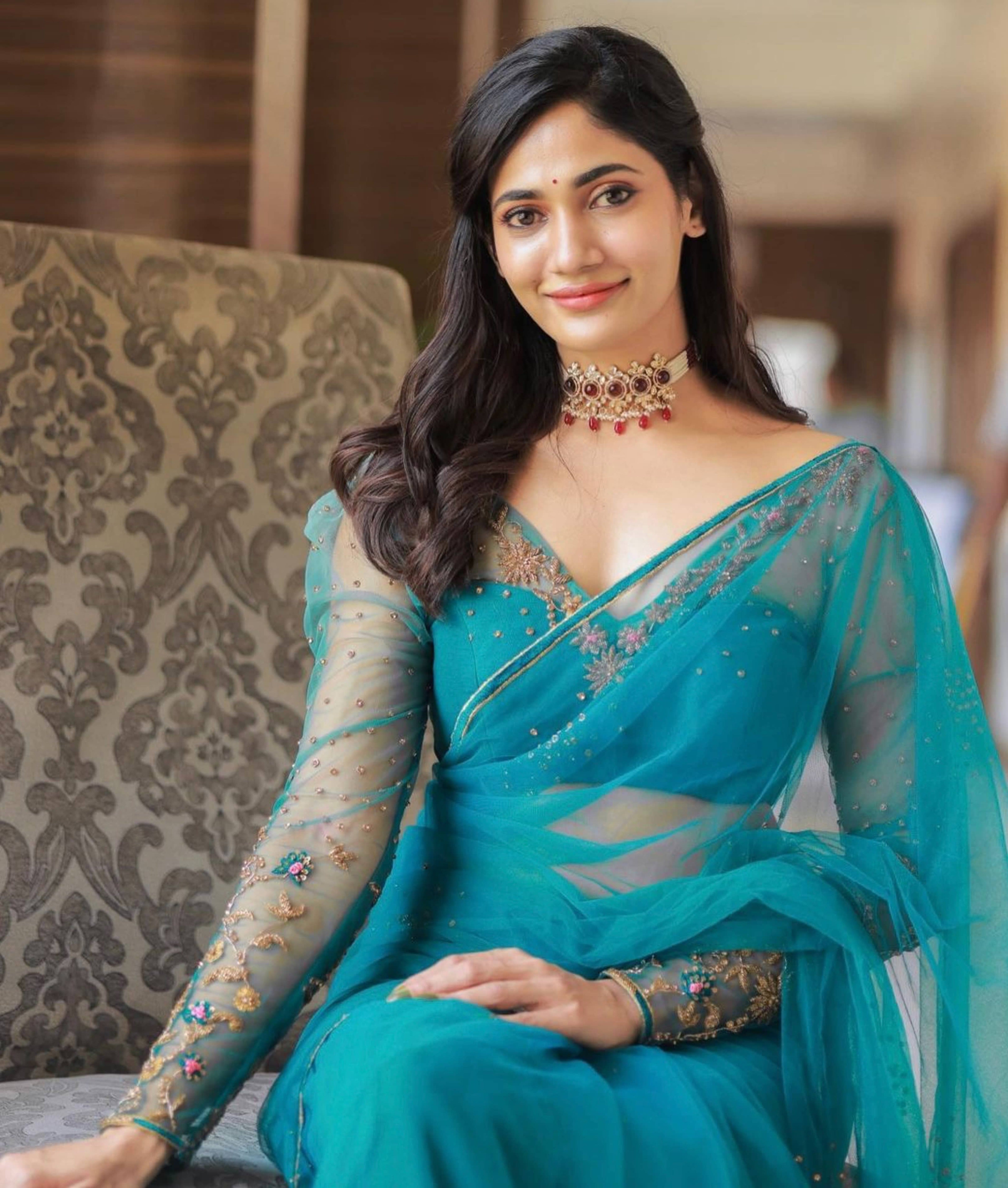 Bigg Boss fame and actress Losliya Mariyanesan in a teal blue handcrafted saree set designed by Archana Karthick. Looking straight at the camera and seated with a smile.