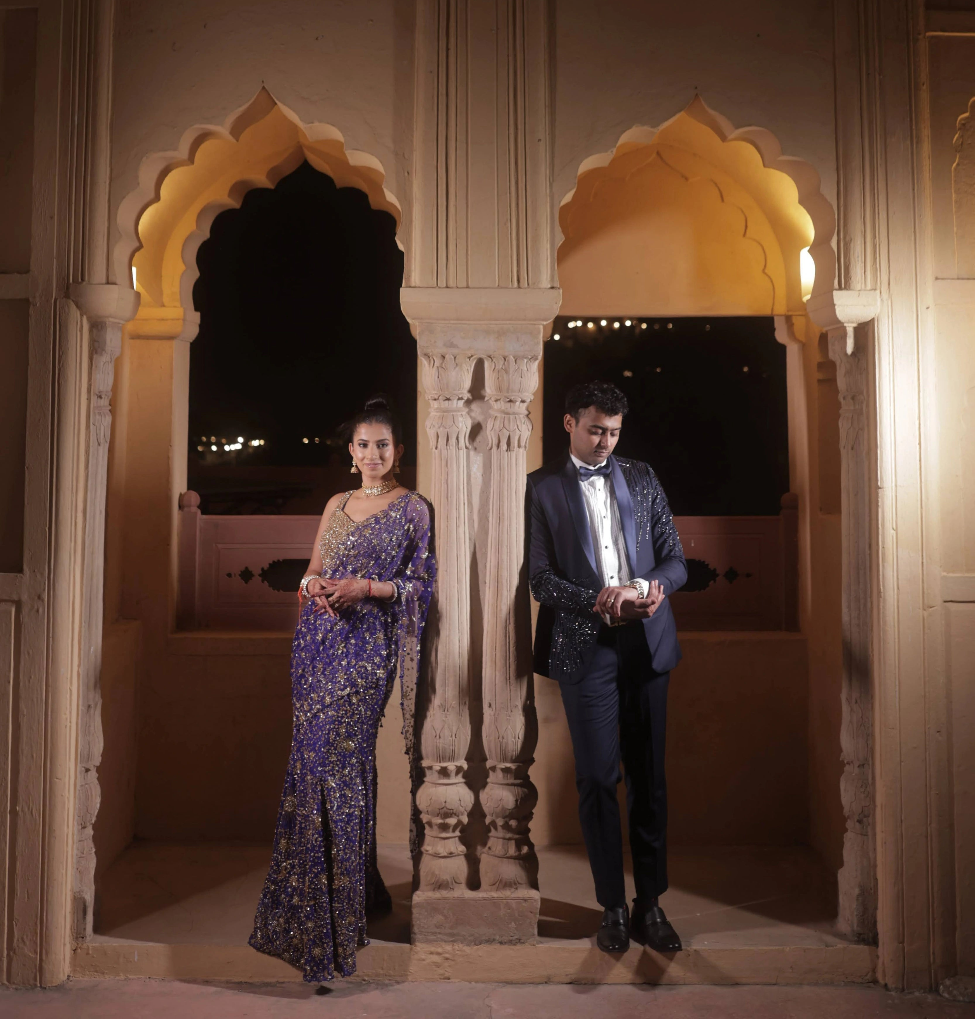 Bride Aashi Pal posing with groom for photoshoot in a midnight blue tulle draped lehenga, handcrafted by team Archana Karthick.