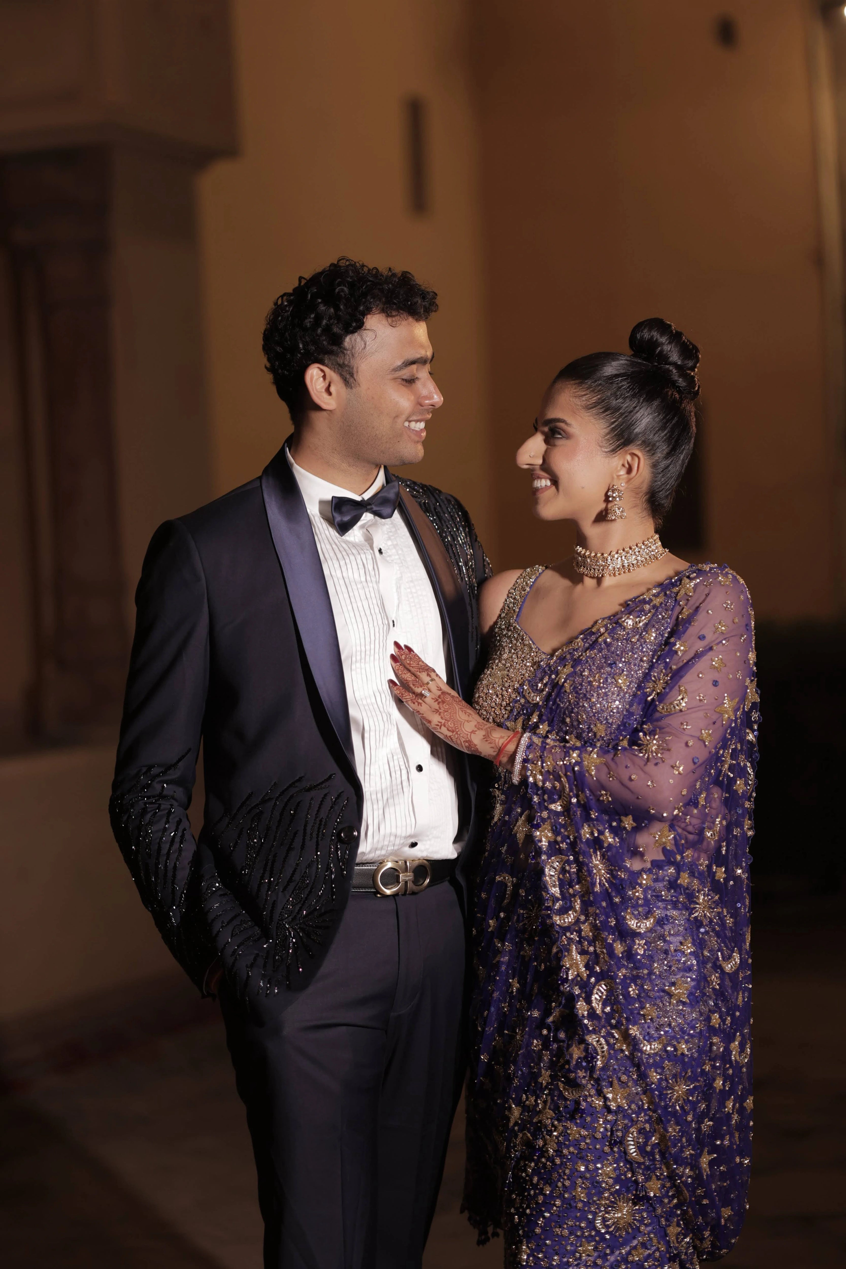 Bride Aashi Pal smiling with groom for photoshoot in a midnight blue tulle draped lehenga, handcrafted by team Archana Karthick.