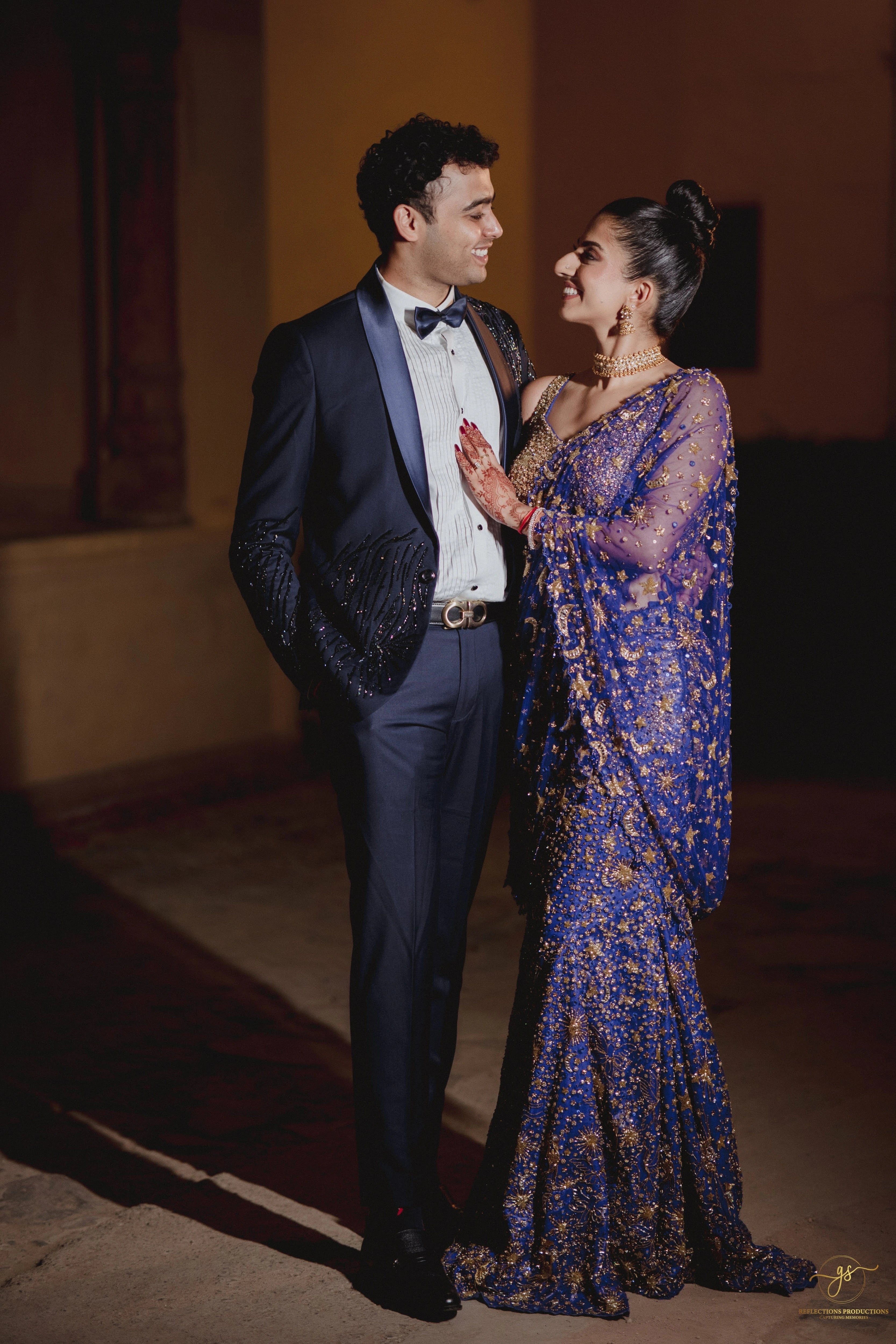 Bride Aashi Pal smiling with groom in a midnight blue tulle draped lehenga, handcrafted by team Archana Karthick.