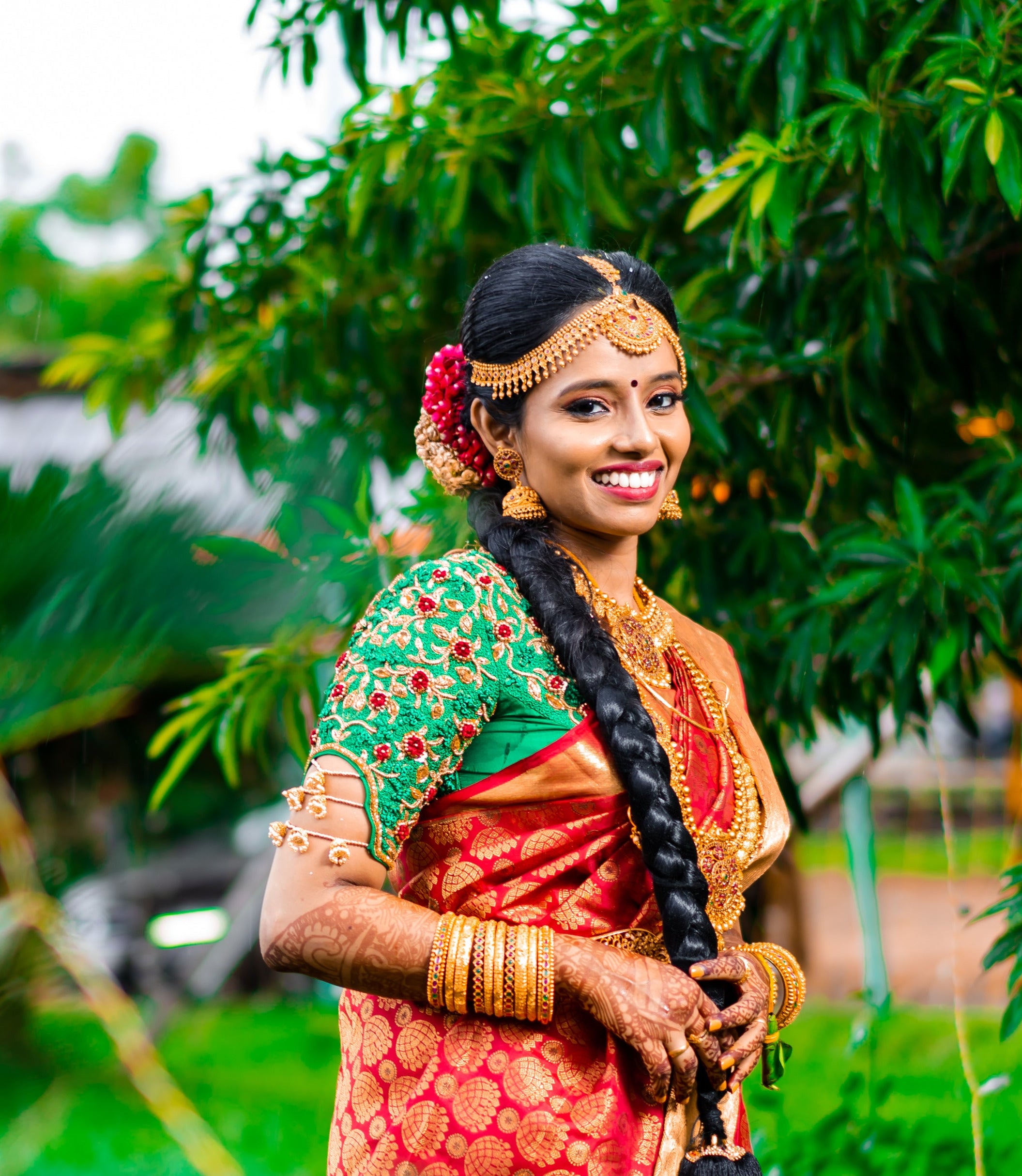 Bride Abhinaya in a handcrafted green raw silk blouse designed by Archana Karthick. Bride is posing in the garden.