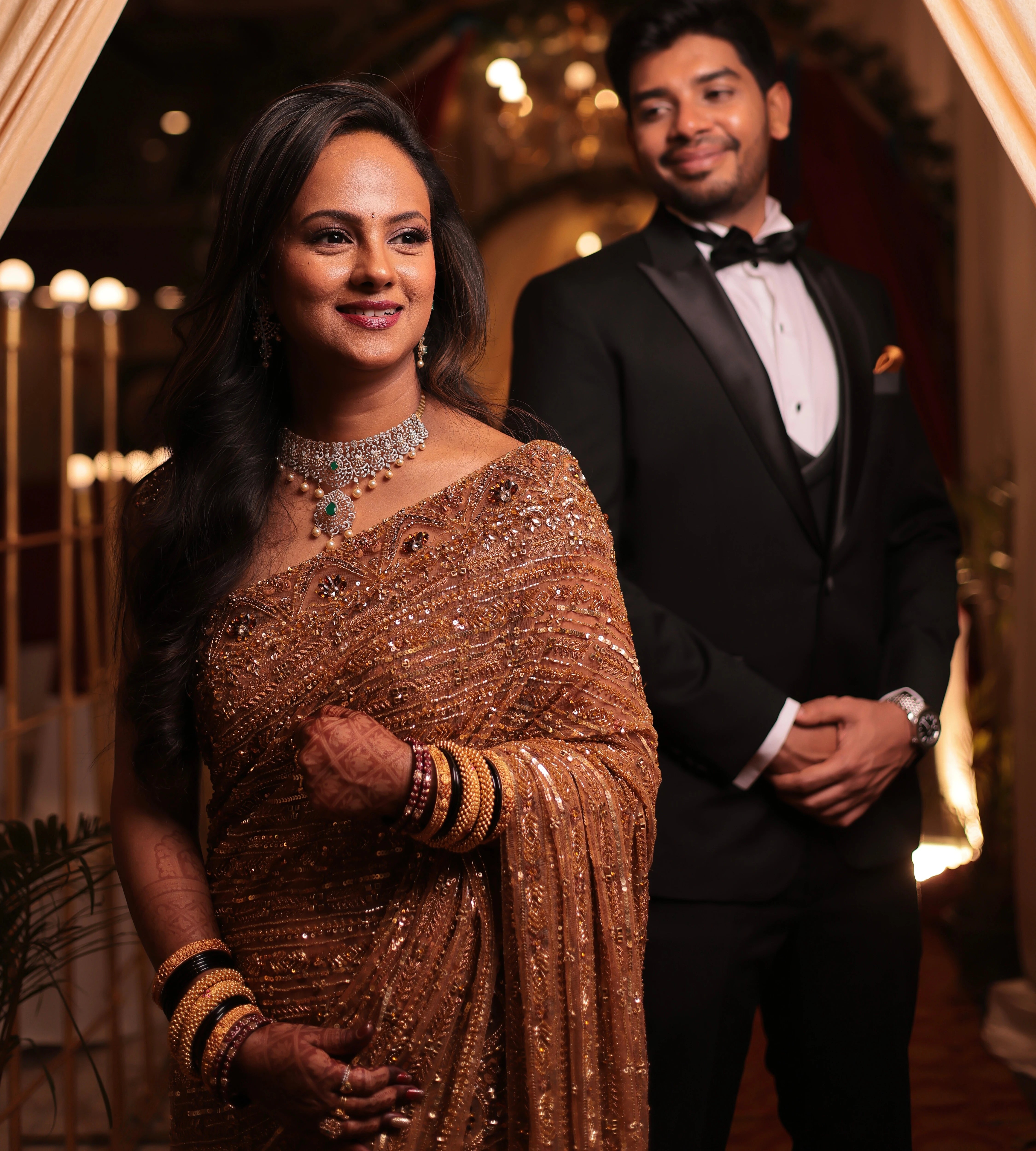 Bride Aishwarya from USA, smiling with groom in a golden tulle saree handcrafted by team Archana Karthick.