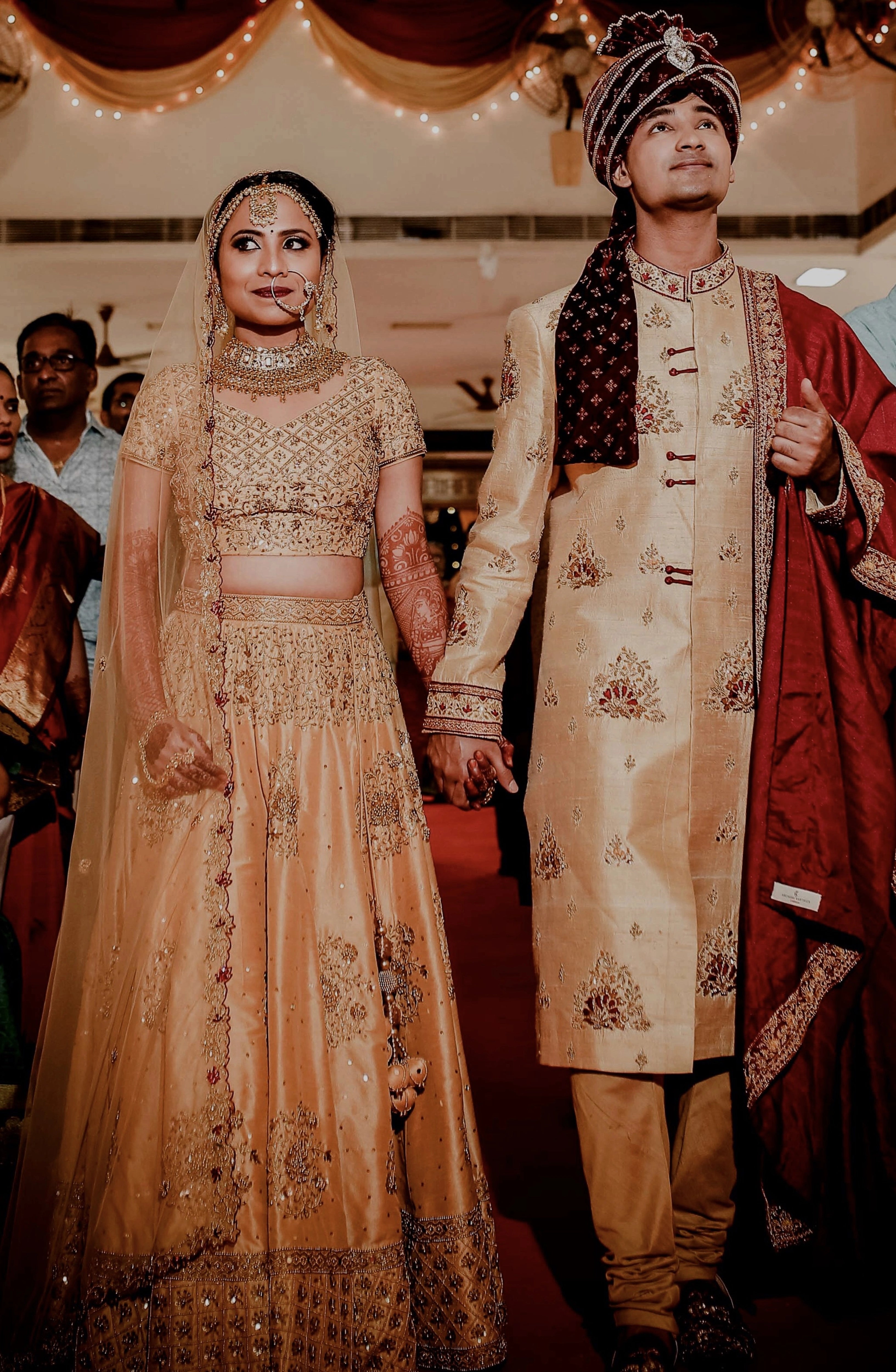 Bride Akshaya and Groom in a gold raw silk lehenga and sherwani, intricately handcrafted with sequins, beads, resham, zardozi by team Archana Karthick.