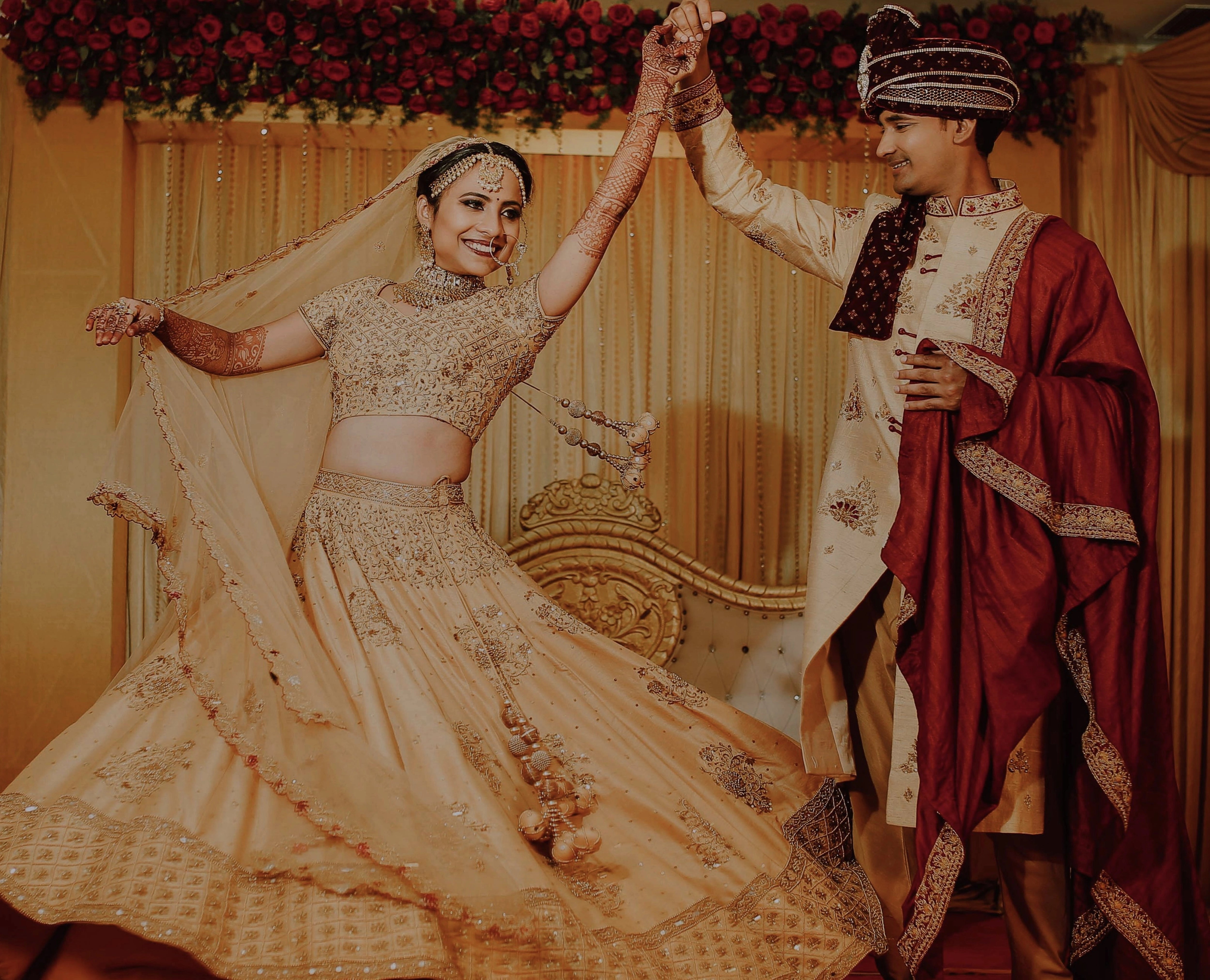 Bride Akshaya and Groom posing in a gold raw silk lehenga and sherwani, intricately handcrafted with sequins, beads, resham, zardozi by team Archana Karthick.