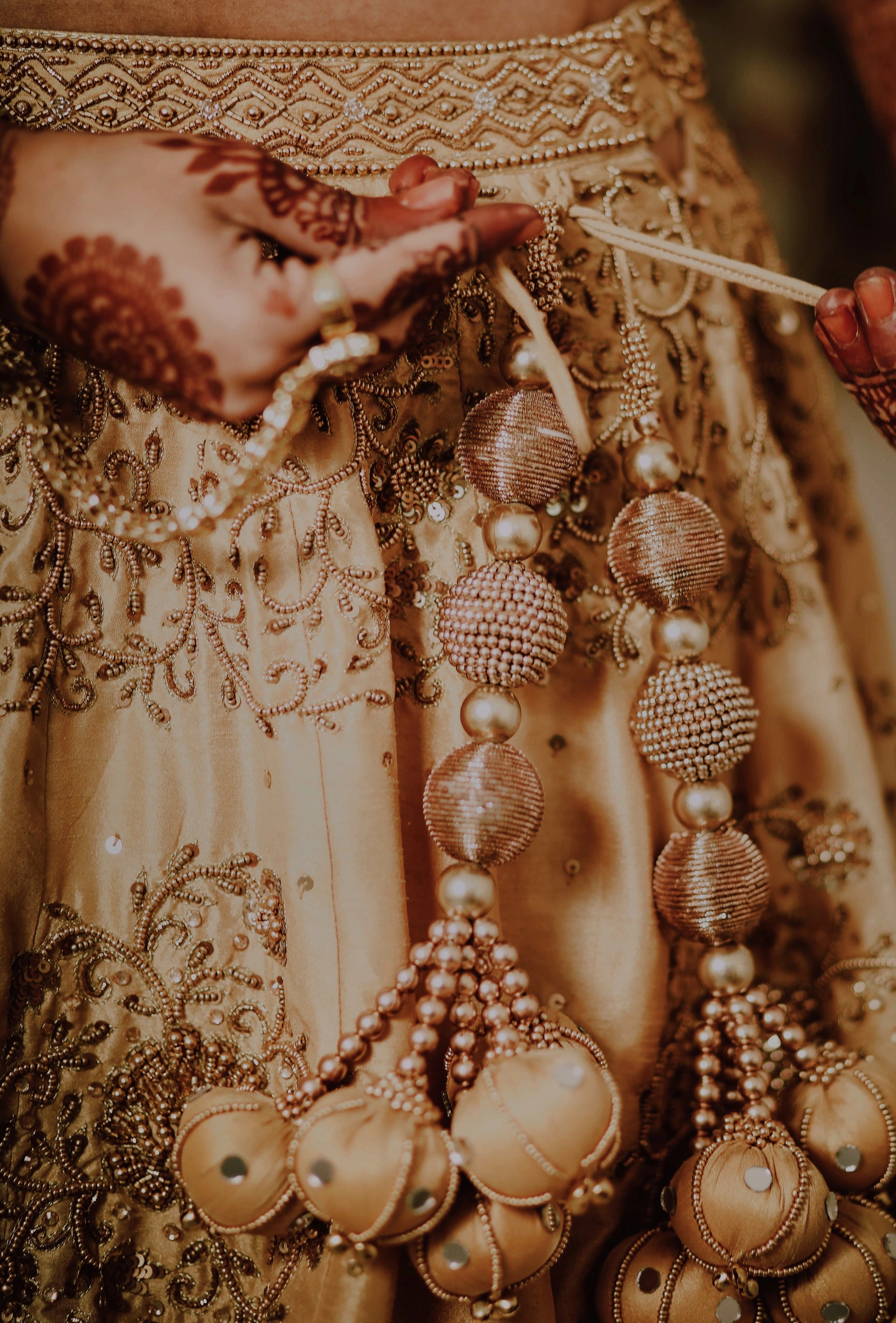 Bride Akshaya showcasing tassels in a gold raw silk lehenga intricately handcrafted with sequins, beads, resham, zardozi by team Archana Karthick.