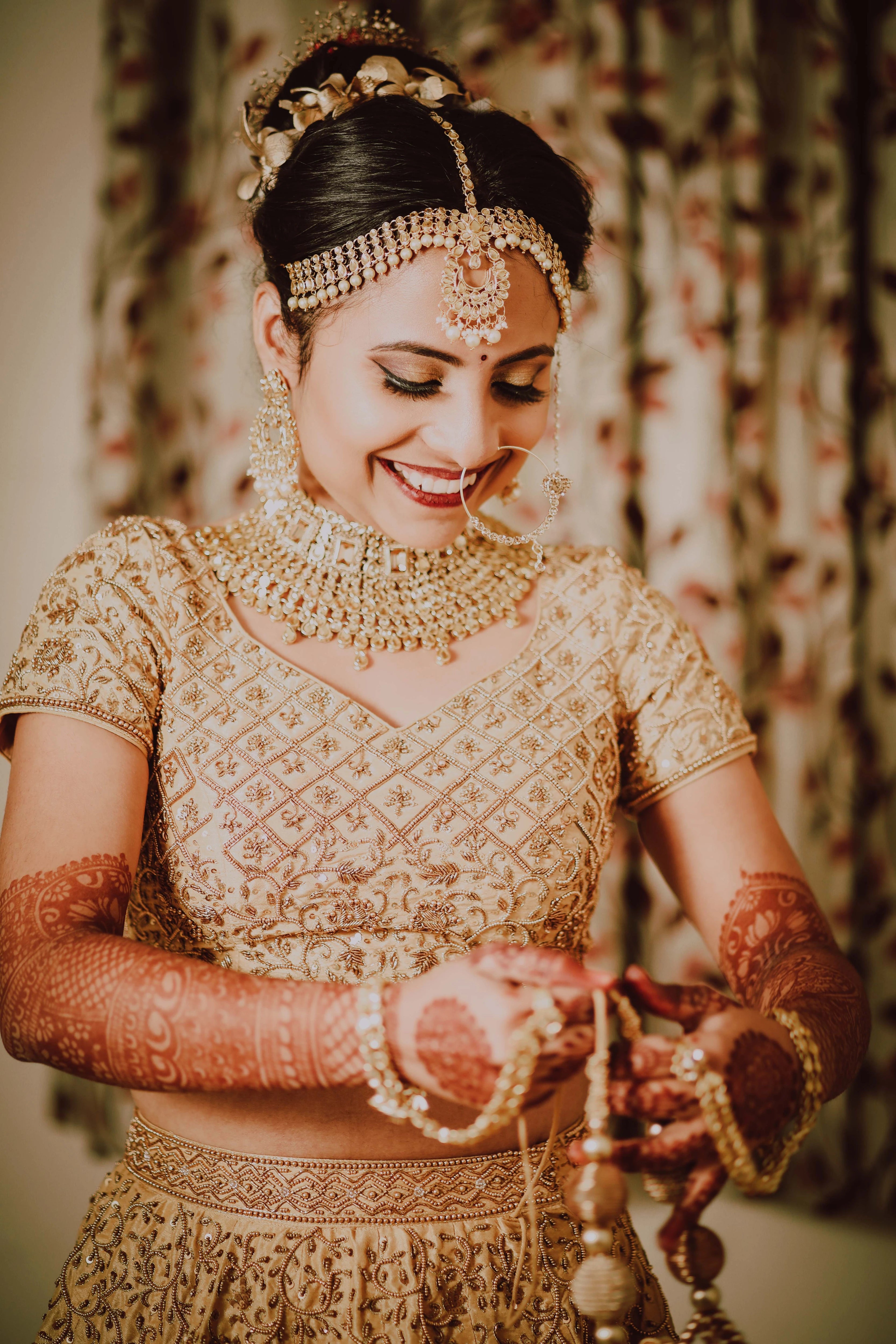 Bride Akshaya smiling in a gold raw silk lehenga and groom in sherwani, intricately handcrafted with sequins, beads, resham, zardozi by team Archana Karthick.