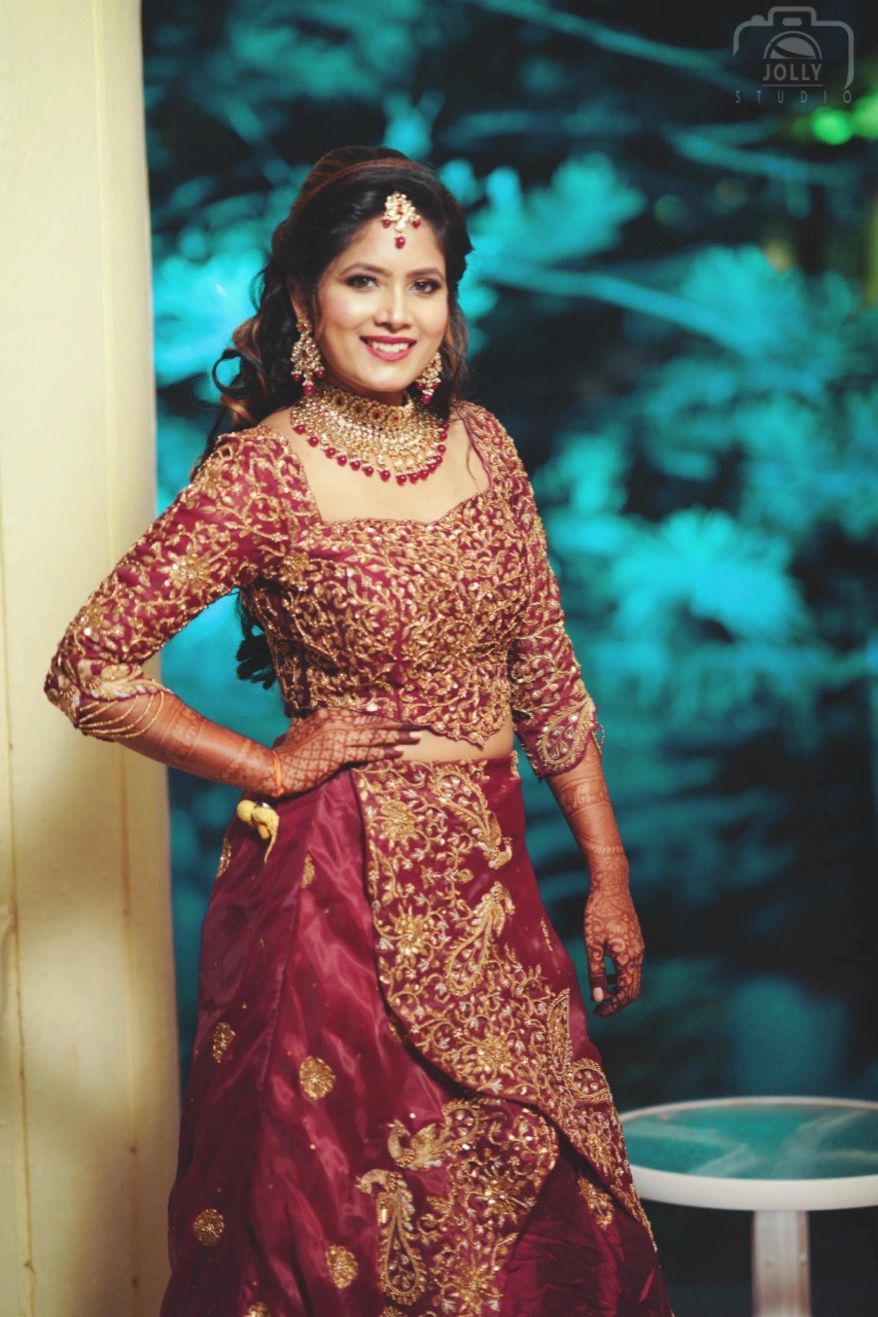 Bride Ankita Singh posing and smiling in a red lehenga intricatelty handcrafted with resham, cutdana, zari and beads by team Archana Karthick.