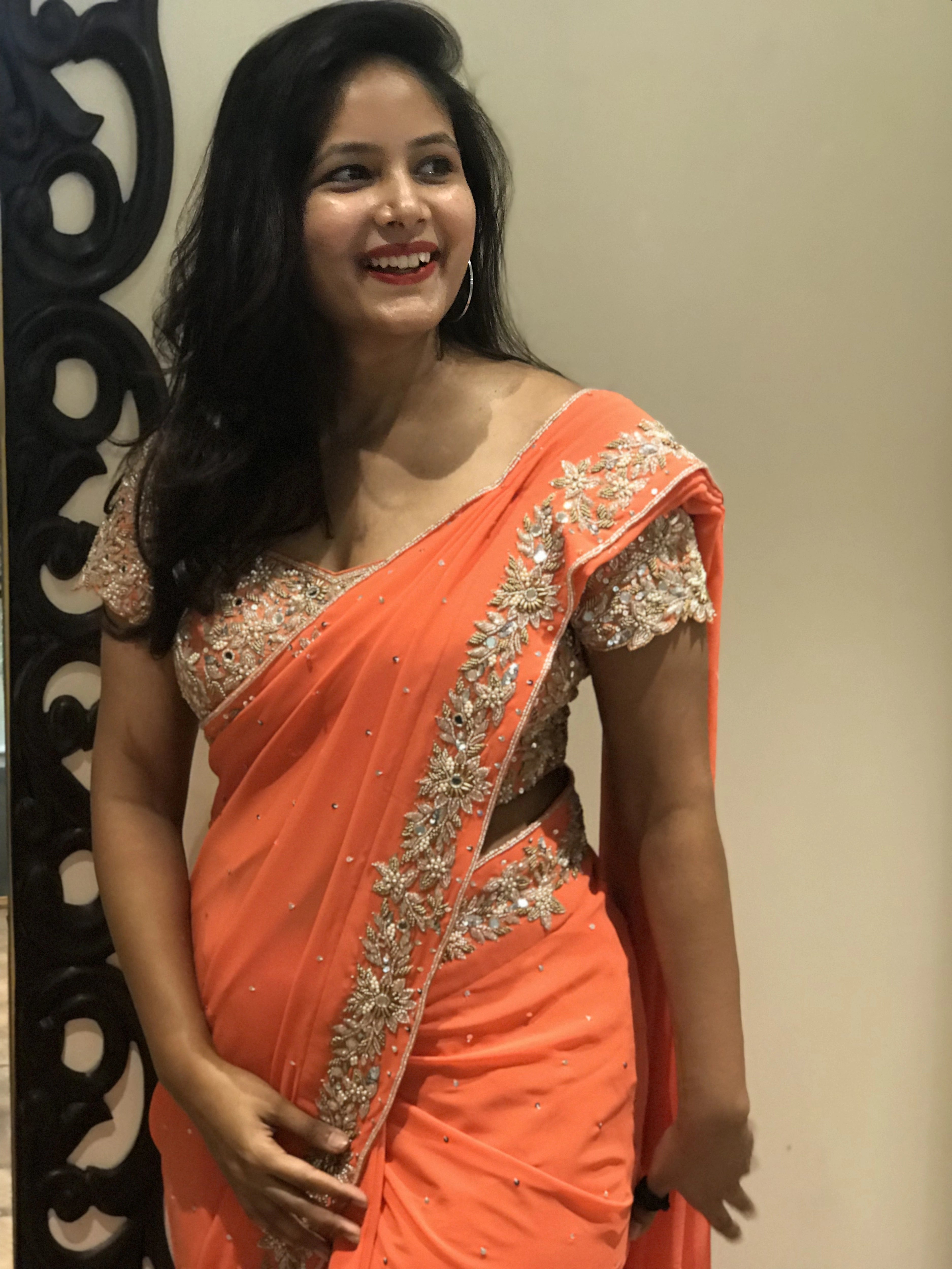 Bride Ankita smiling in an orange georgette saree and blouse handcrafted by team Archana Karthick.