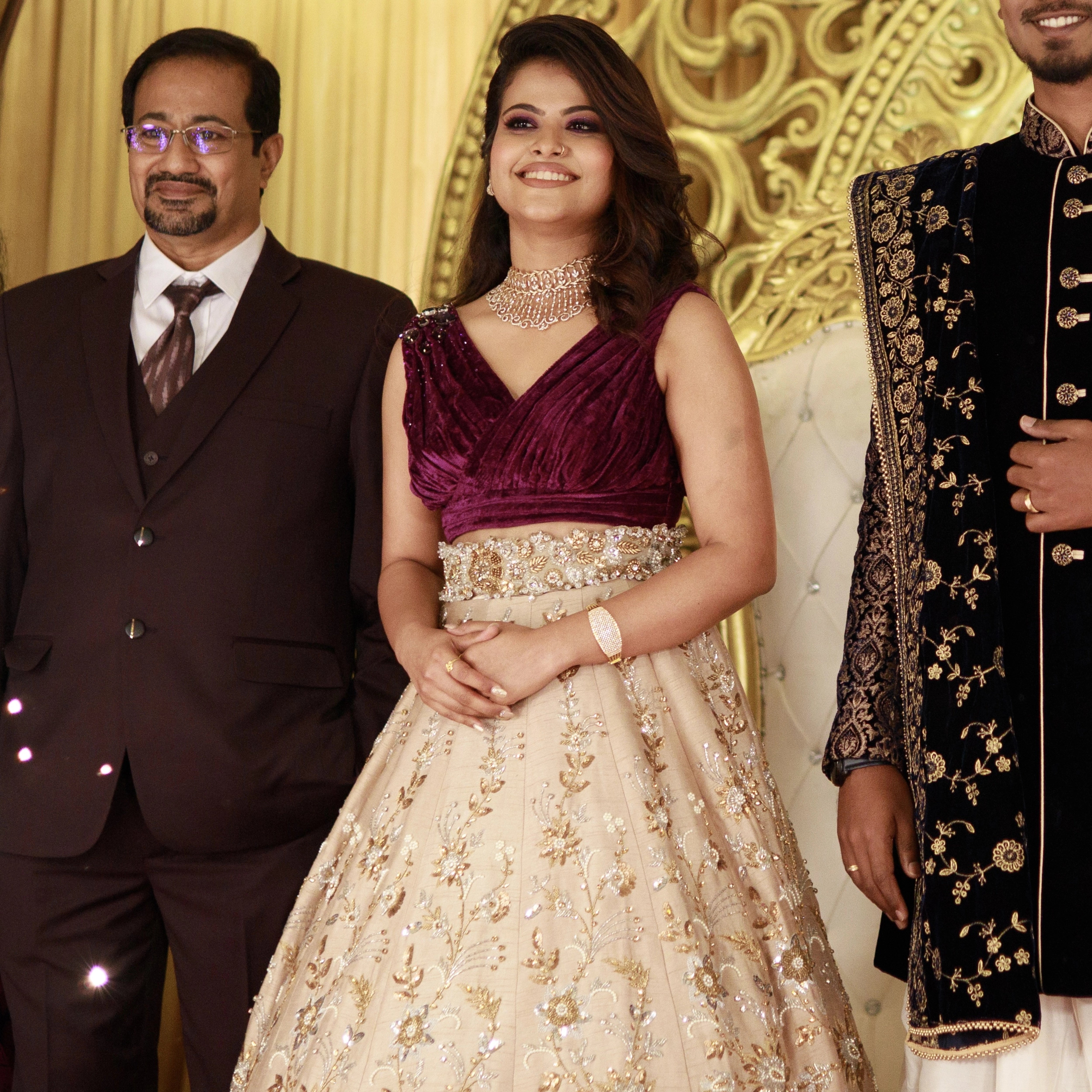 Bride Anu from Kerala posing with groom in a purple & beige lehenga, handcrafted by team Archana Karthick.