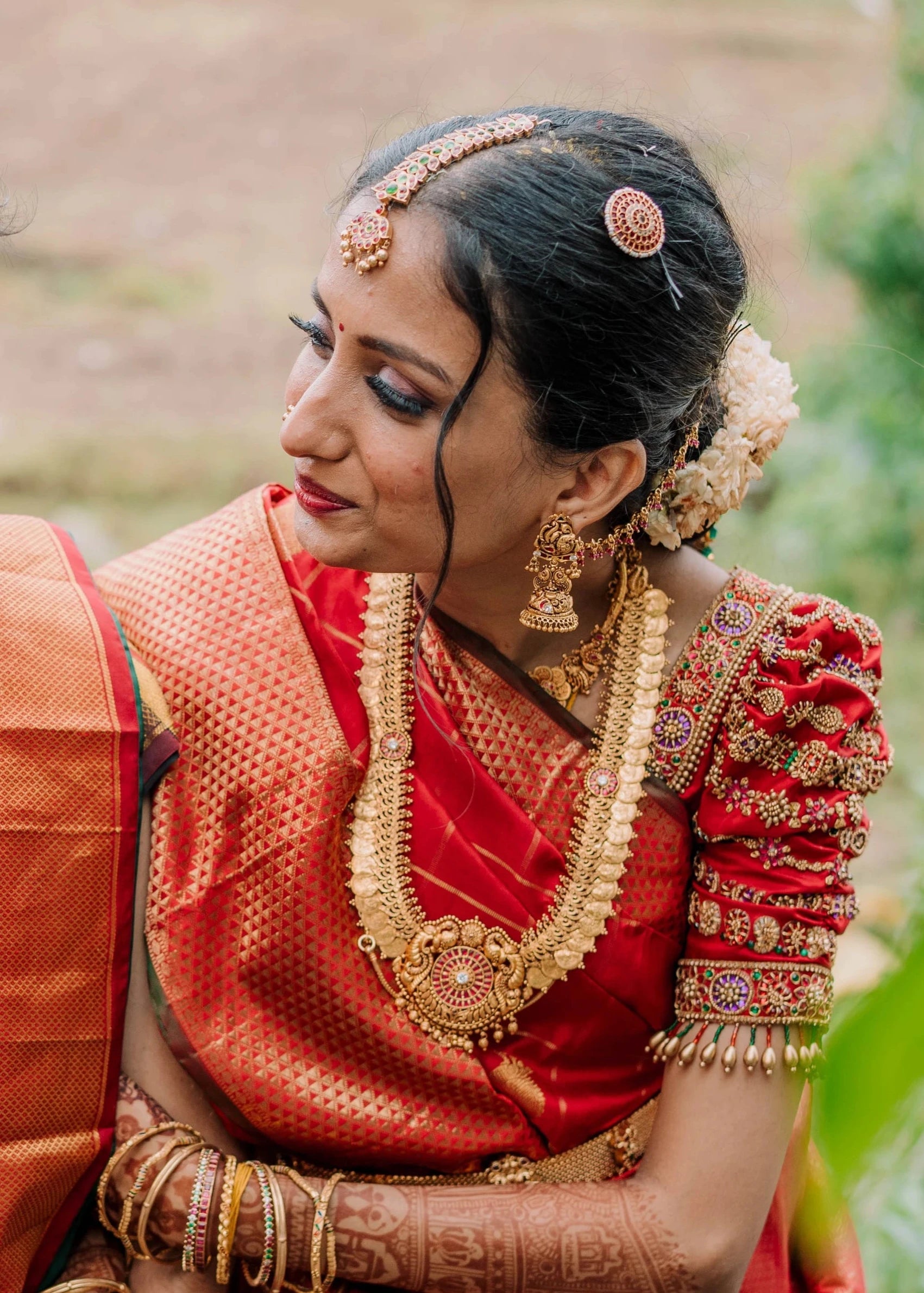 Bride Anusha K smiling in a red concept silk puff sleeved blouse, intricately handcrafted with zardosi, beads, kundan, and kemp stones by team Archana Karthick.
