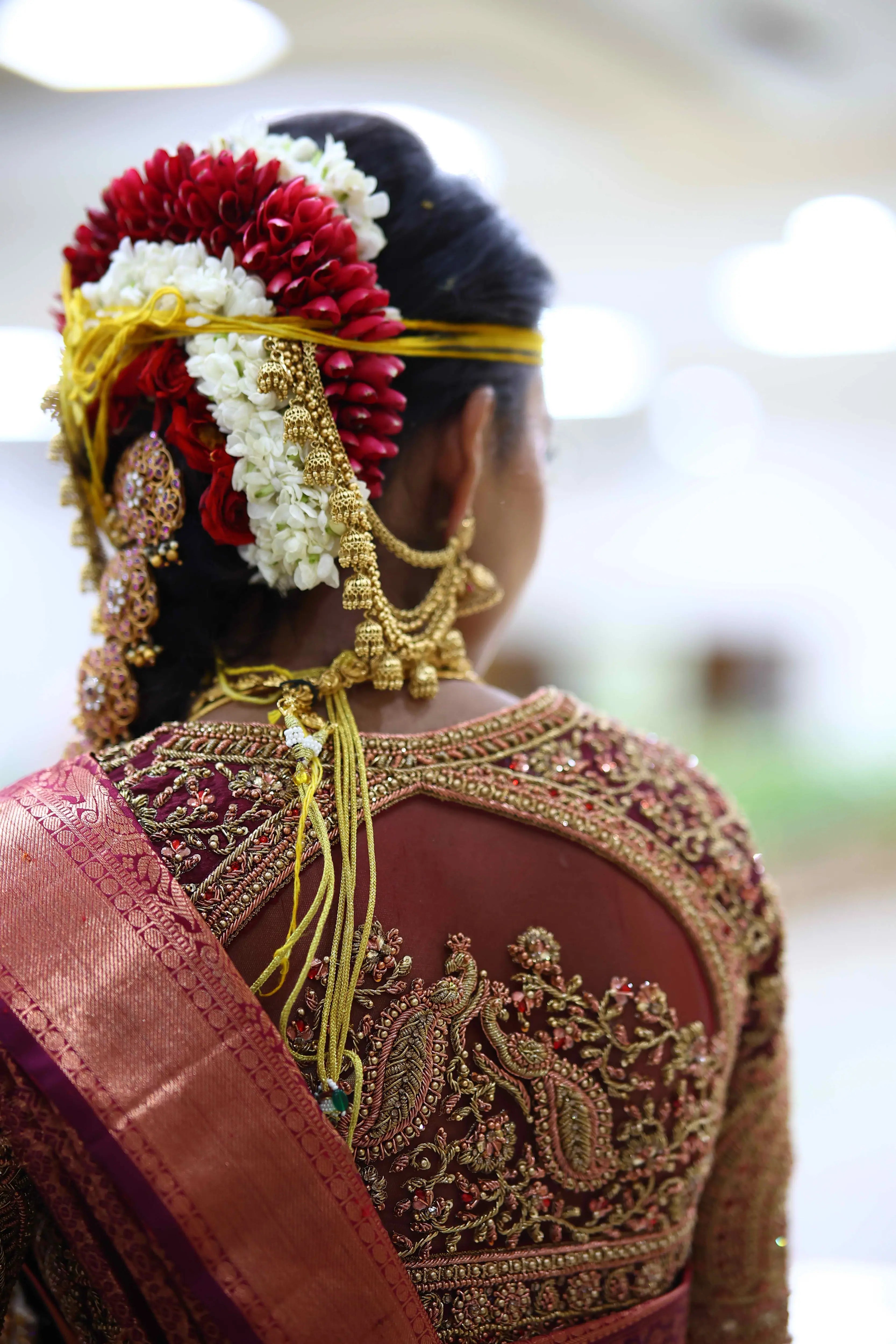 Bride Ashwathi from Dindigul posing again in a maroon concept silk blouse, intricately handcrafted with zardosi, beads, kundan, sequins and kemp stones by team Archana Karthick.