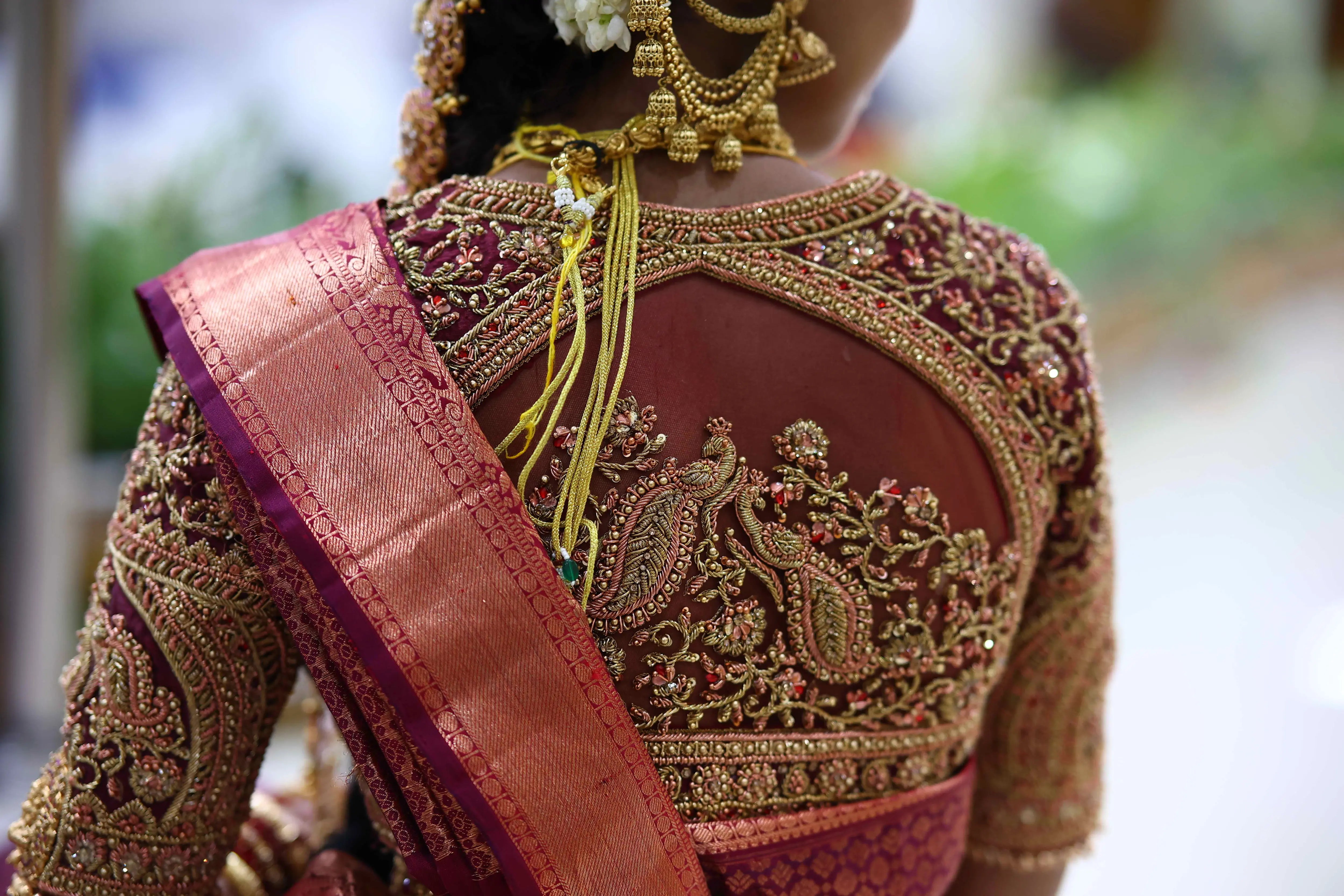 Bride Ashwathi from Dindigul showcasing back blouse design in a maroon concept silk blouse, intricately handcrafted with zardosi, beads, kundan, sequins and kemp stones by team Archana Karthick.