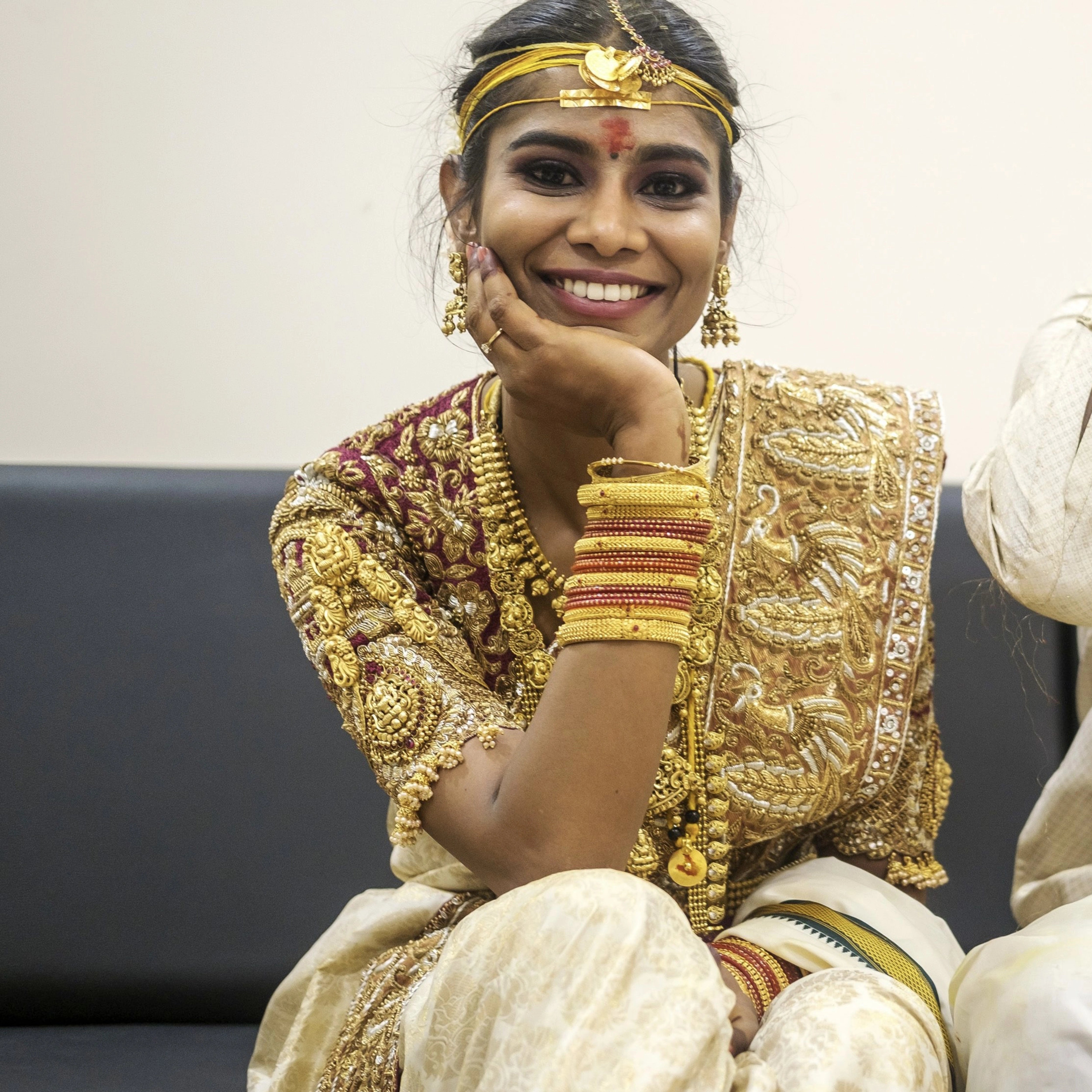 Bride Bhargavi smiling at the camera in a maroon palanquin concept silk blouse and saree border, intricately handcrafted with zardosi, beads, resham work, kundan and sequins by team Archana Karthick.